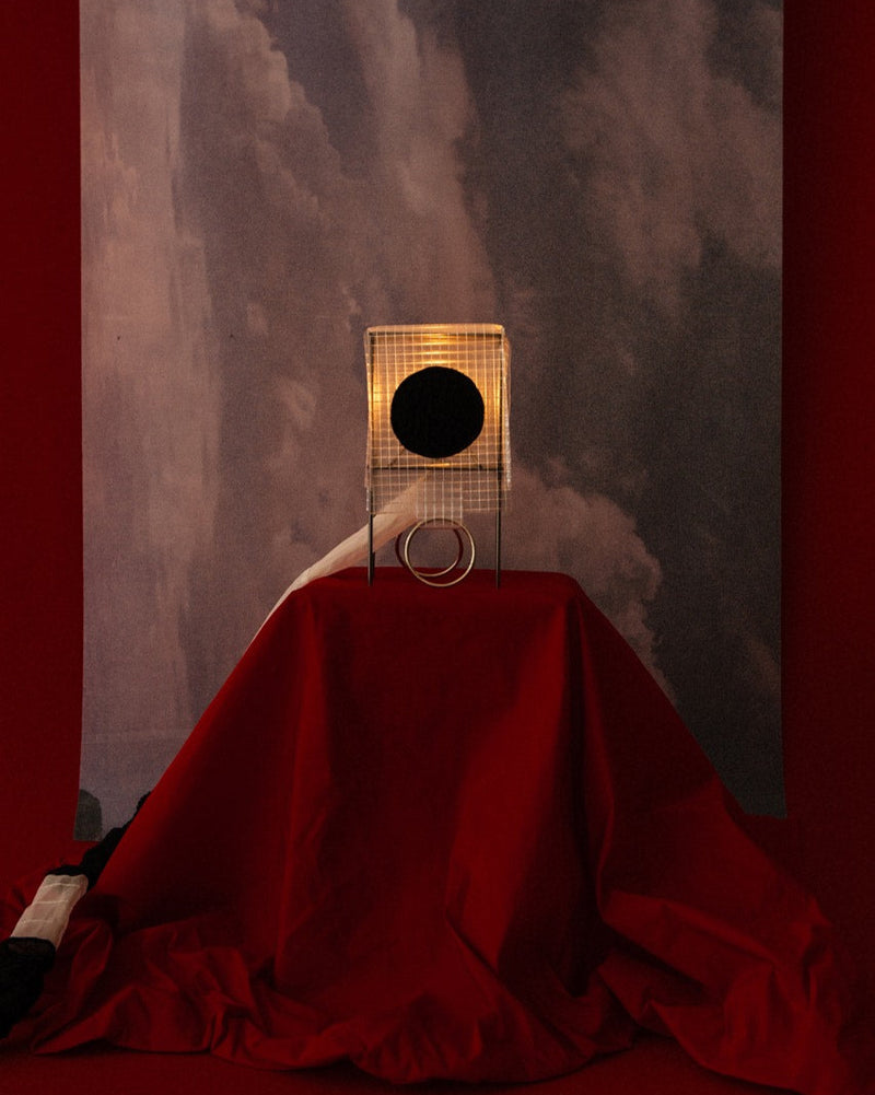 Geometric cage table lamp with red fabric drape against marble backdrop