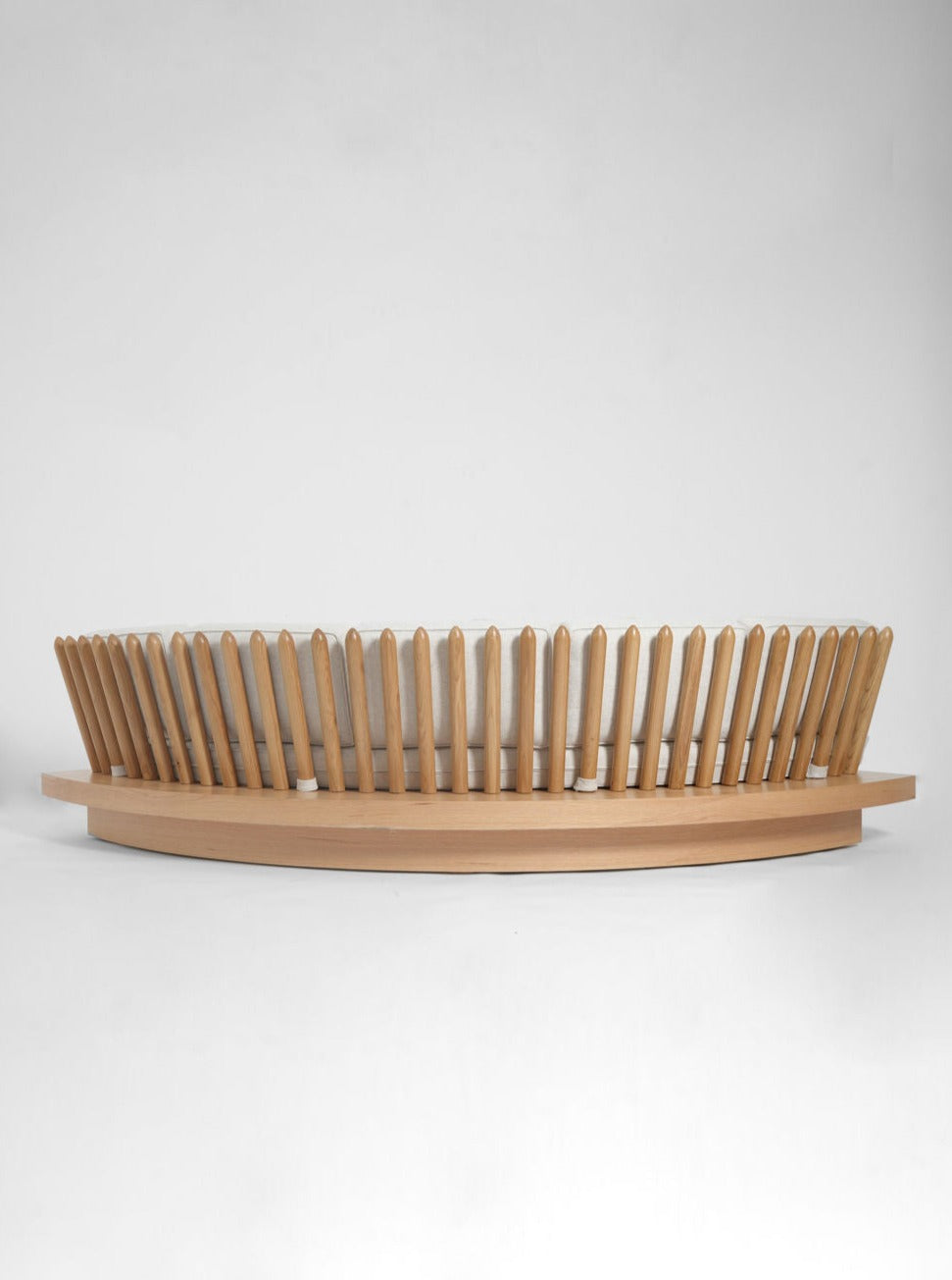 A round wooden coffee table with vertical slats surrounds a flat, circular top, perfect for pairing with the Barracuda Interiors San Romano Round Oak Sofa, set against a plain white background.