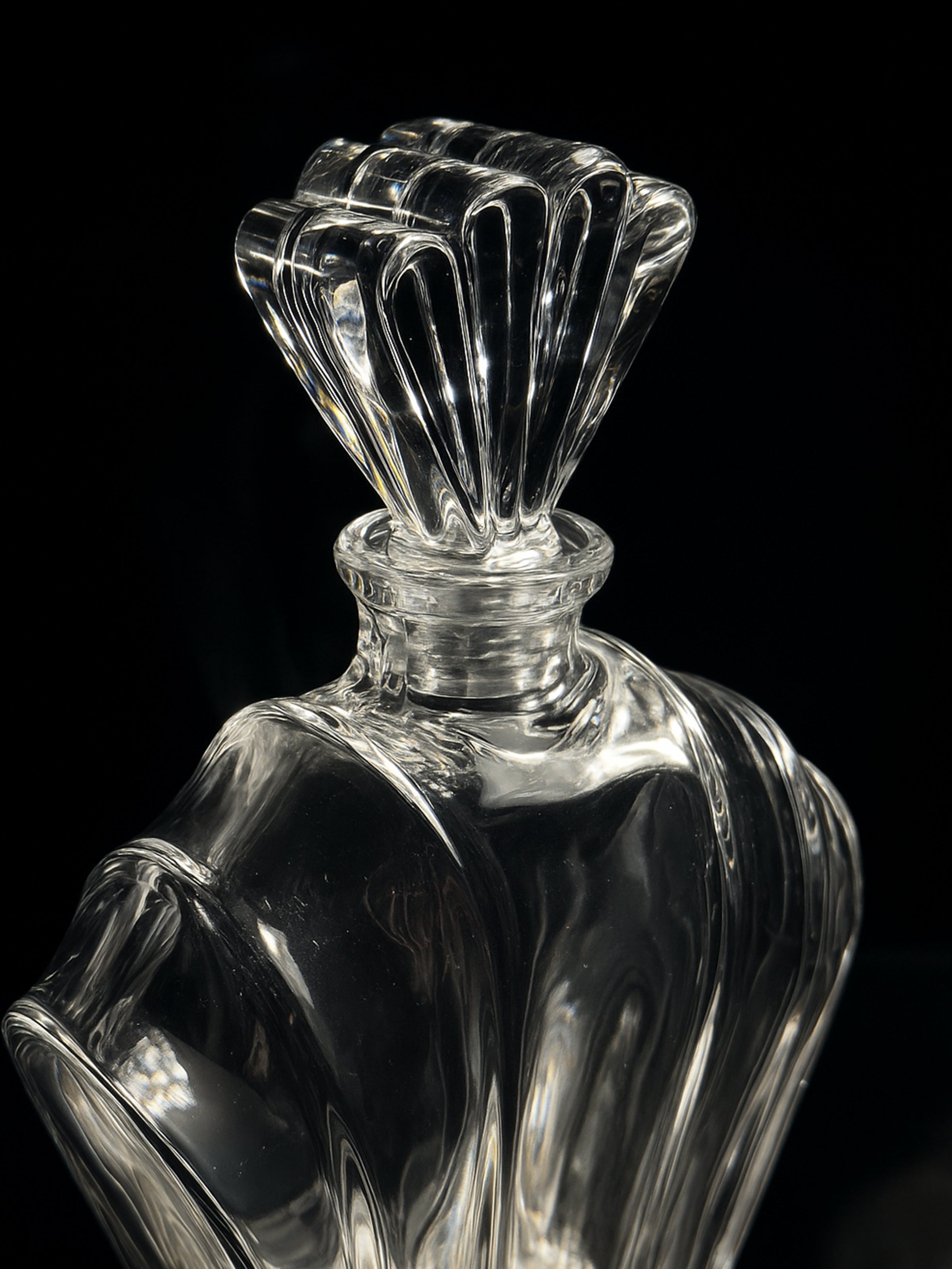 A close-up of the Italian crystal Glass Art Deco Decanter by Dodo Vintage (1980s) shows its elegant, faceted stopper and curves reflecting light against a black backdrop, highlighting its intricate, vintage design.