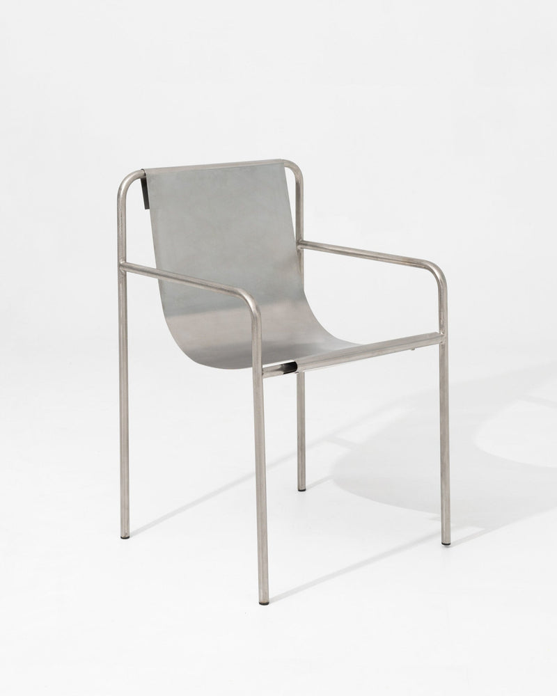 The DESSERT chair by SALAK features a curved seat and backrest with slim tubular armrests and legs, creating a sculptural, minimalistic piece ideal for modern interiors.