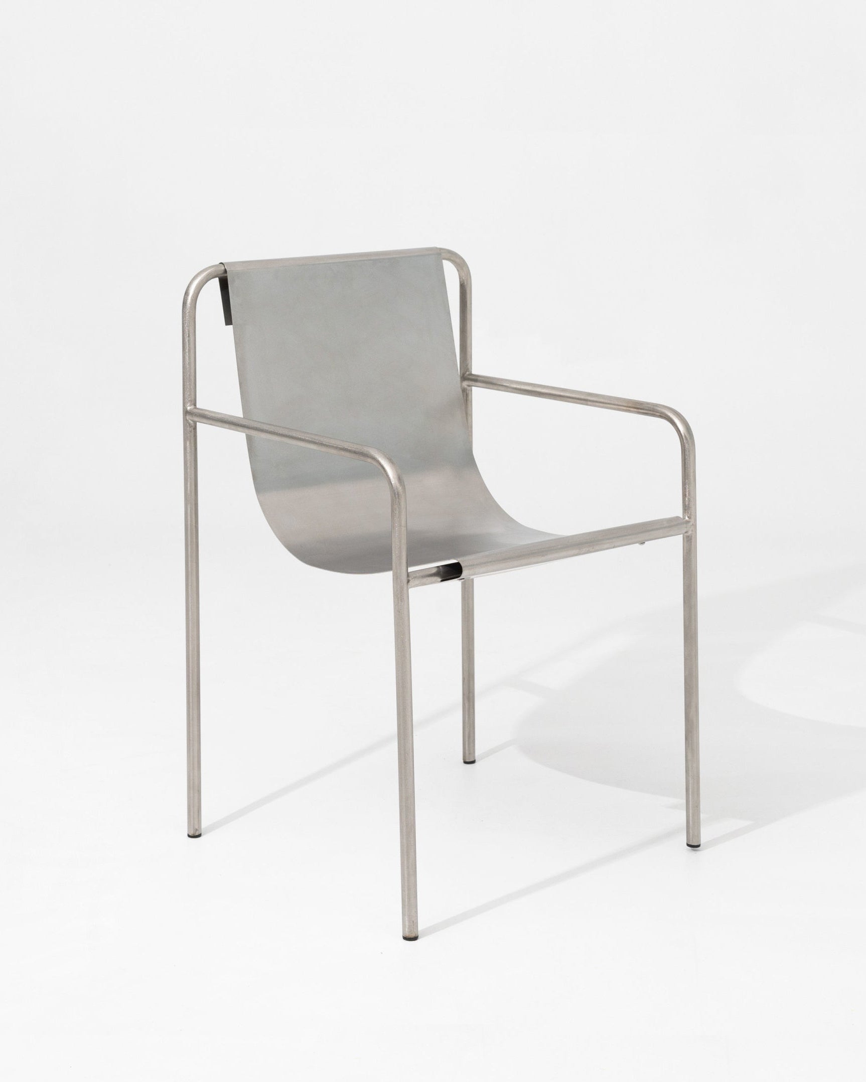 The DESSERT chair by SALAK features a curved seat and backrest with slim tubular armrests and legs, creating a sculptural, minimalistic piece ideal for modern interiors.