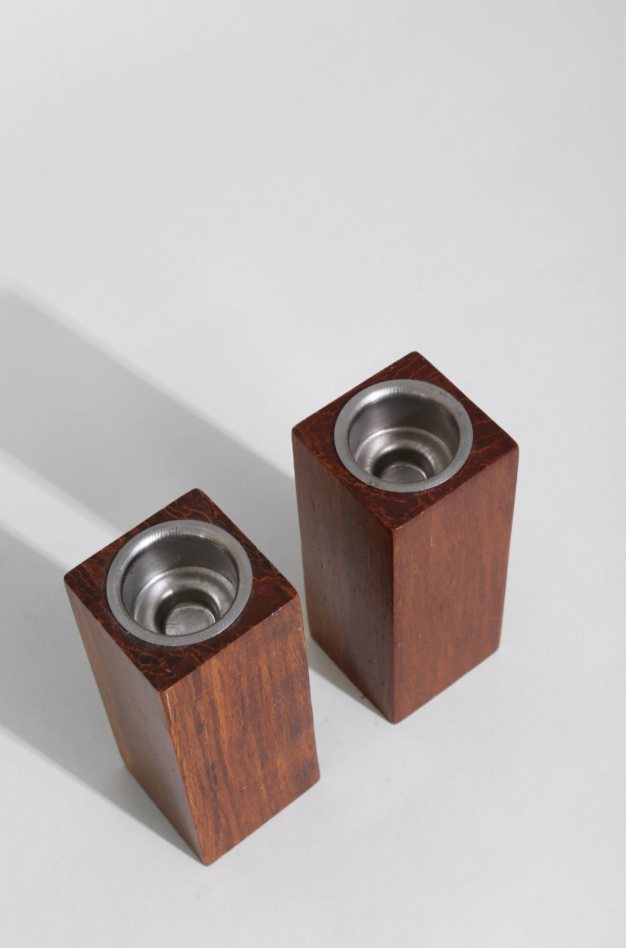 Two walnut wood block candleholders with metal inserts on white surface