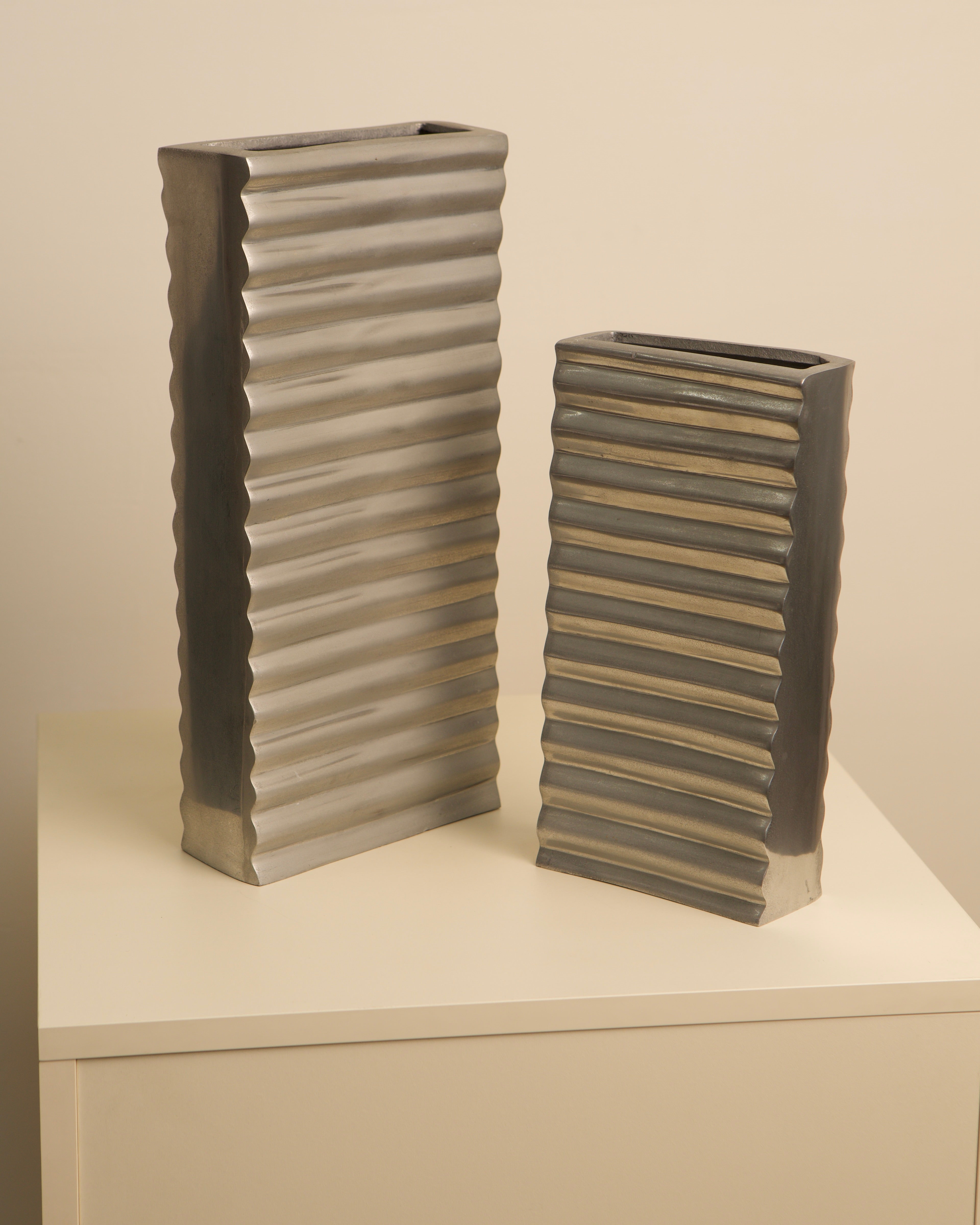 Pair of Italian ribbed aluminum vases on white display shelf