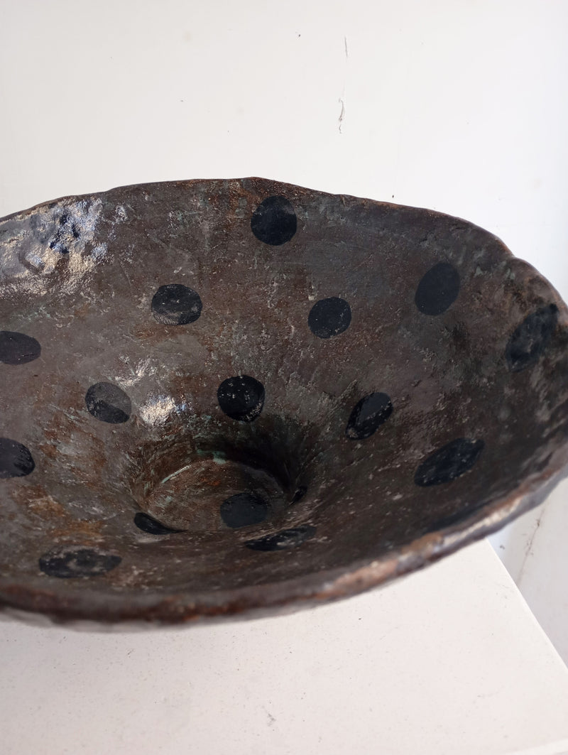 The Coupe 40 by Claire Pain is a handmade, one-of-a-kind dark ceramic bowl featuring a slightly uneven rim, glossy enamel, and black polka dots inside, displayed on a plain white background.
