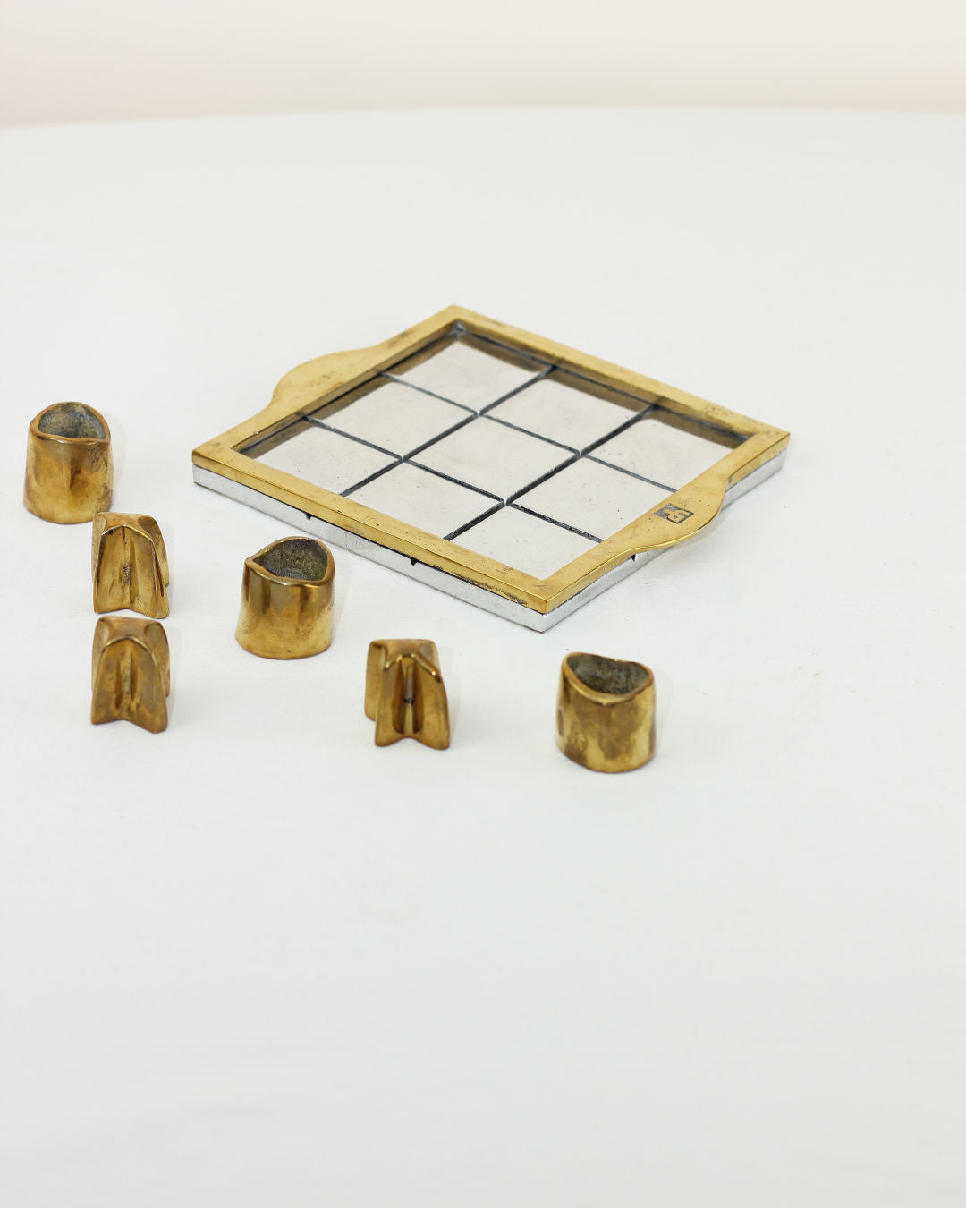Brutalist Tic Tac Toe — side angle showing brass game pieces on white surface