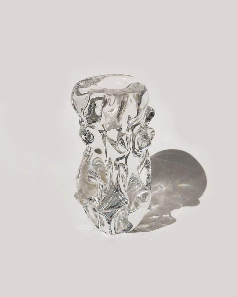 The Les Objoies Organic Glass Candle Holder, featuring a sculptural biomorphic design with abstract, swirling forms, rests on a light surface and casts a gentle shadow to the right.