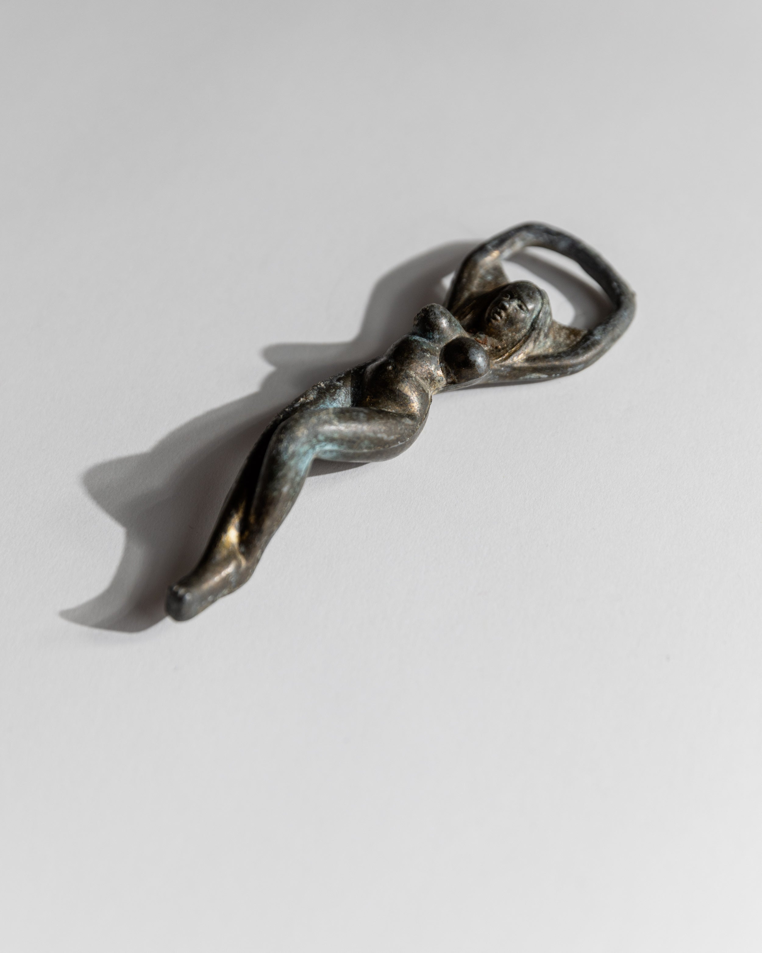 Vintage 1940s Bottle Opener Brass, Nude Woman Shape — back view on white surface
