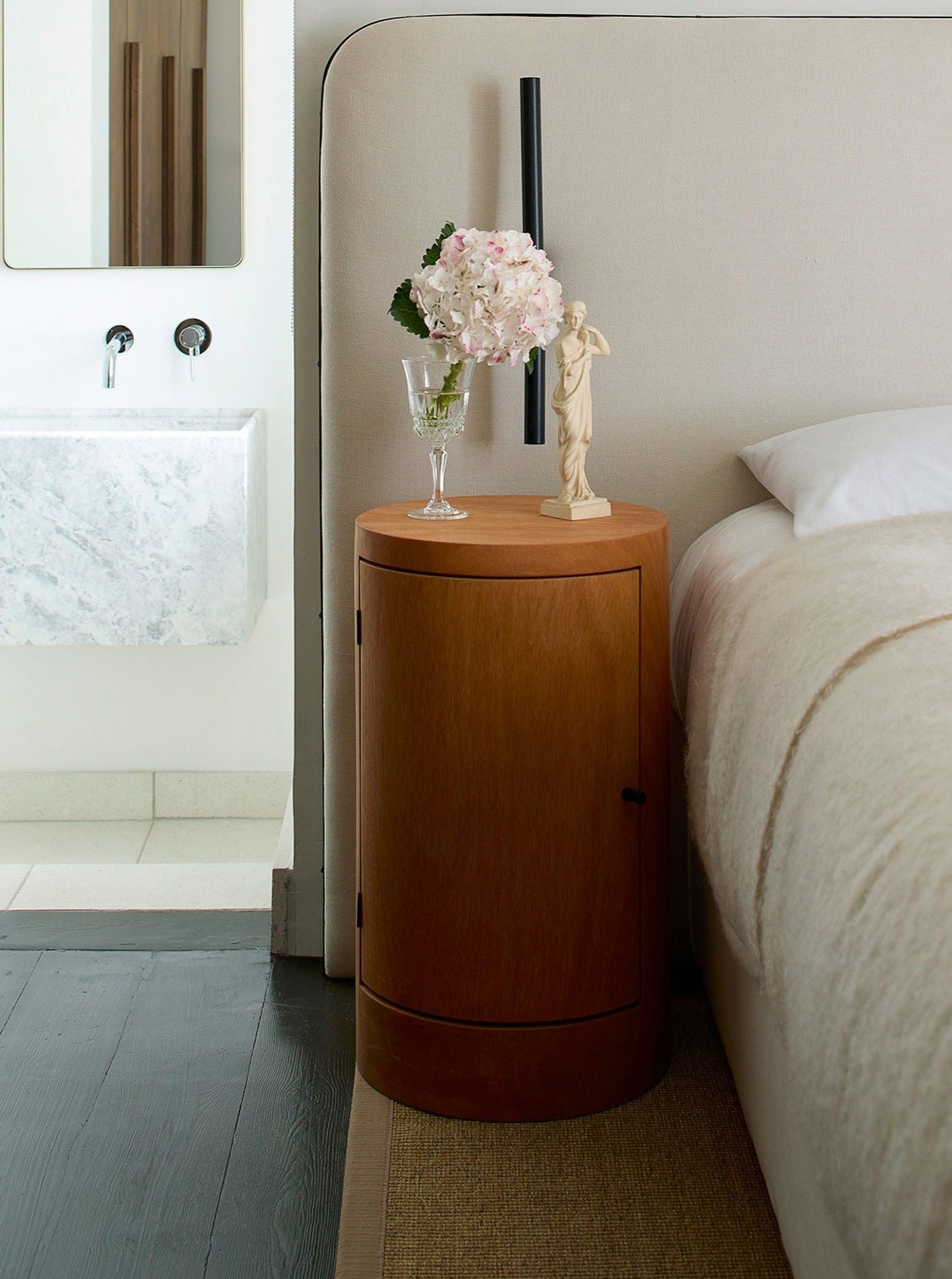Pair of Constant Nightstand in Oiled Iroko — angled view beside bed with decor