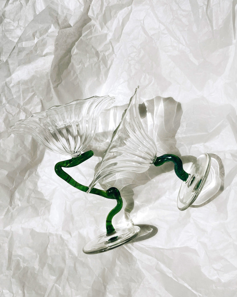 Clear glass ice cups with green twisted stems on white fabric backdrop