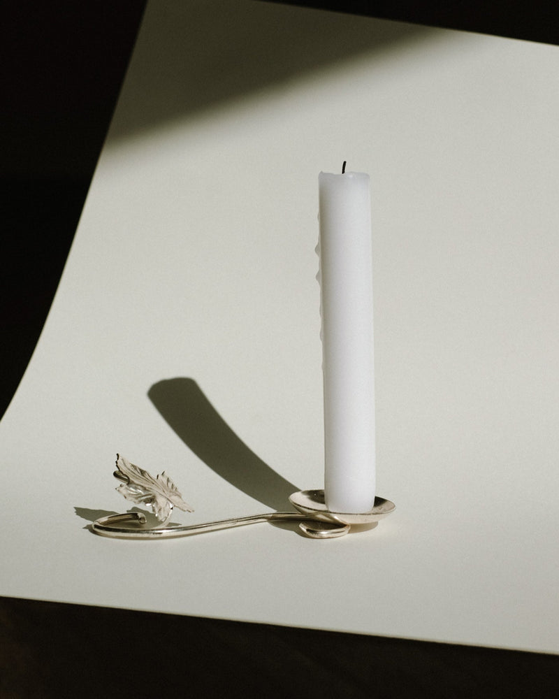 Silver-plated candle holder with feather detail on white surface