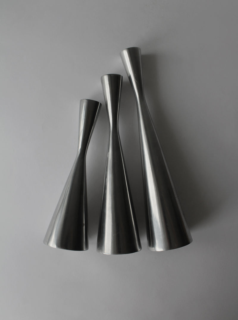 Three polished aluminum candle holders with curved hourglass silhouettes