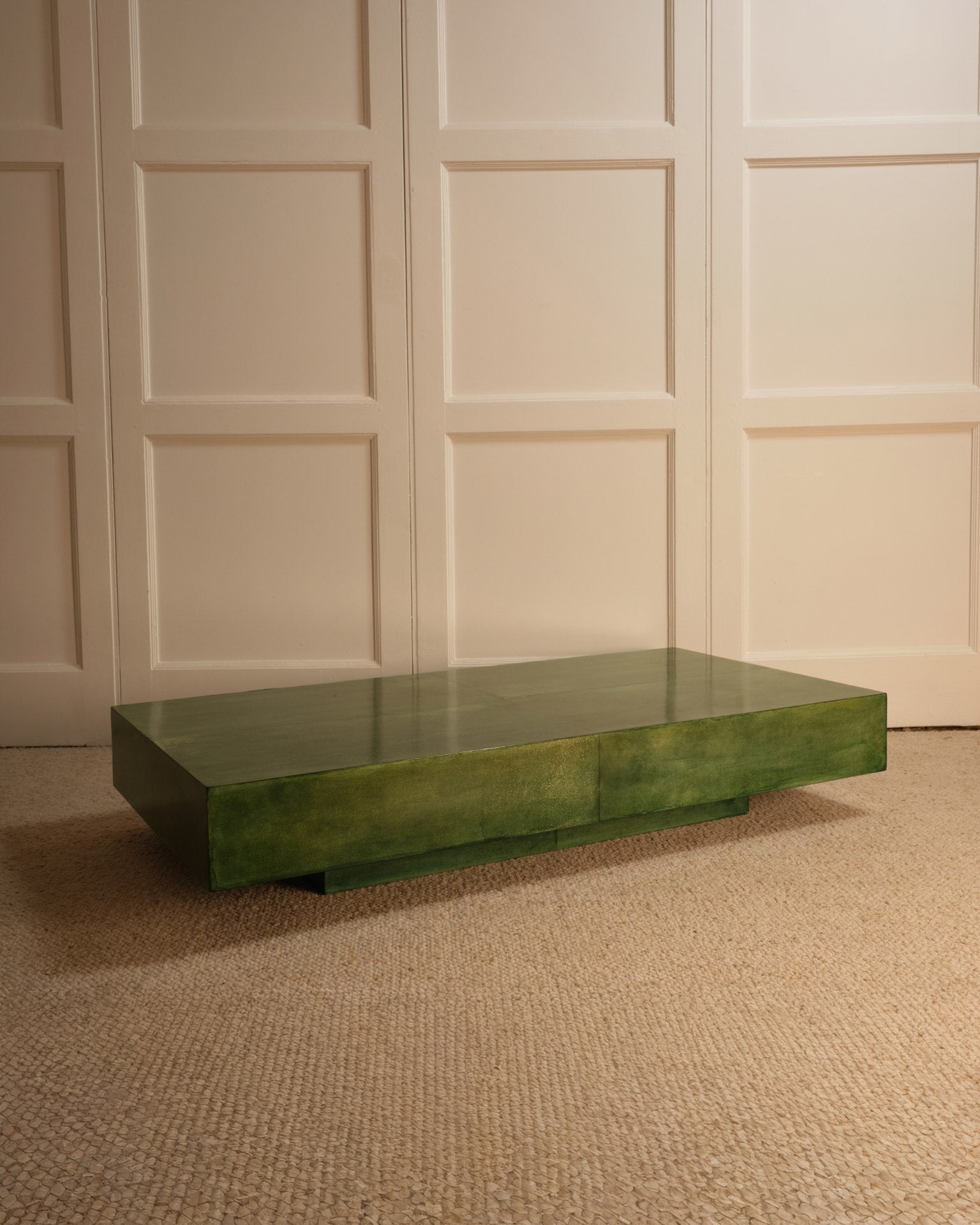 The Green Parchment Table by Galerie Vauvart, a rectangular Italian coffee table with a glossy green parchment finish, sits on a textured beige carpet in front of a cream-paneled wall.