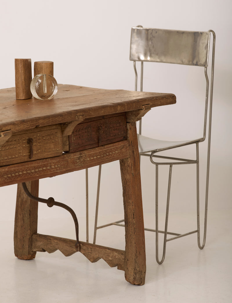 Spanish Folk Vernacular Table From The 17th Century — close-up of rustic wooden surface with metal chair