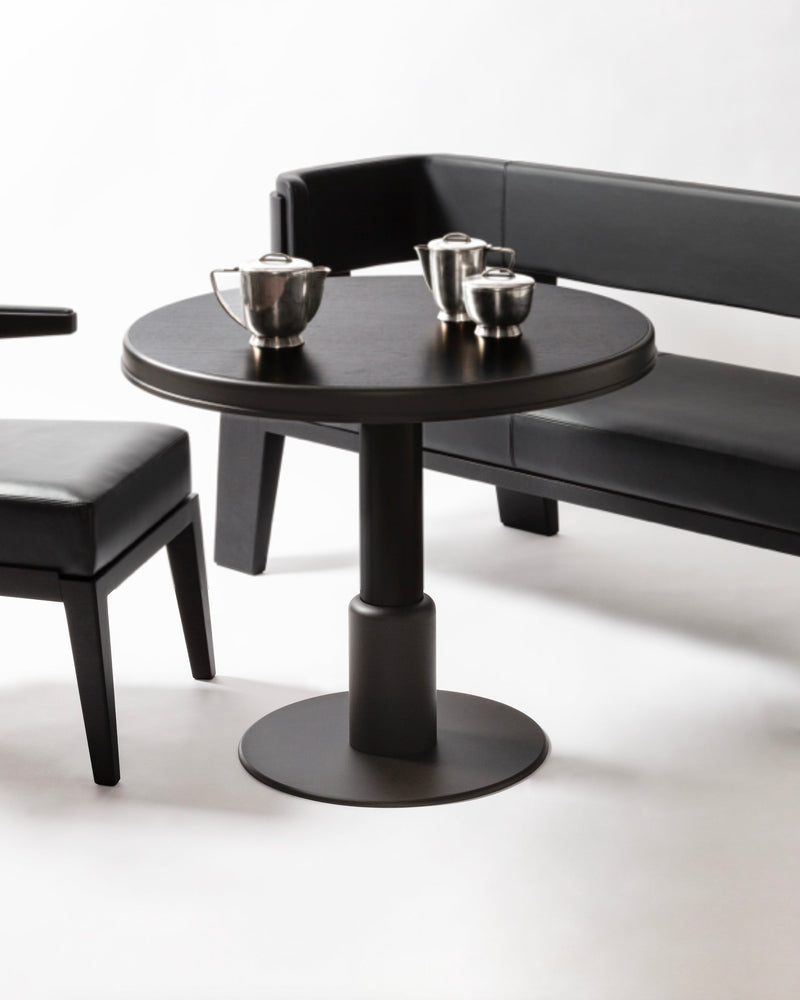 Round black dining table with pedestal base and metallic tea service set