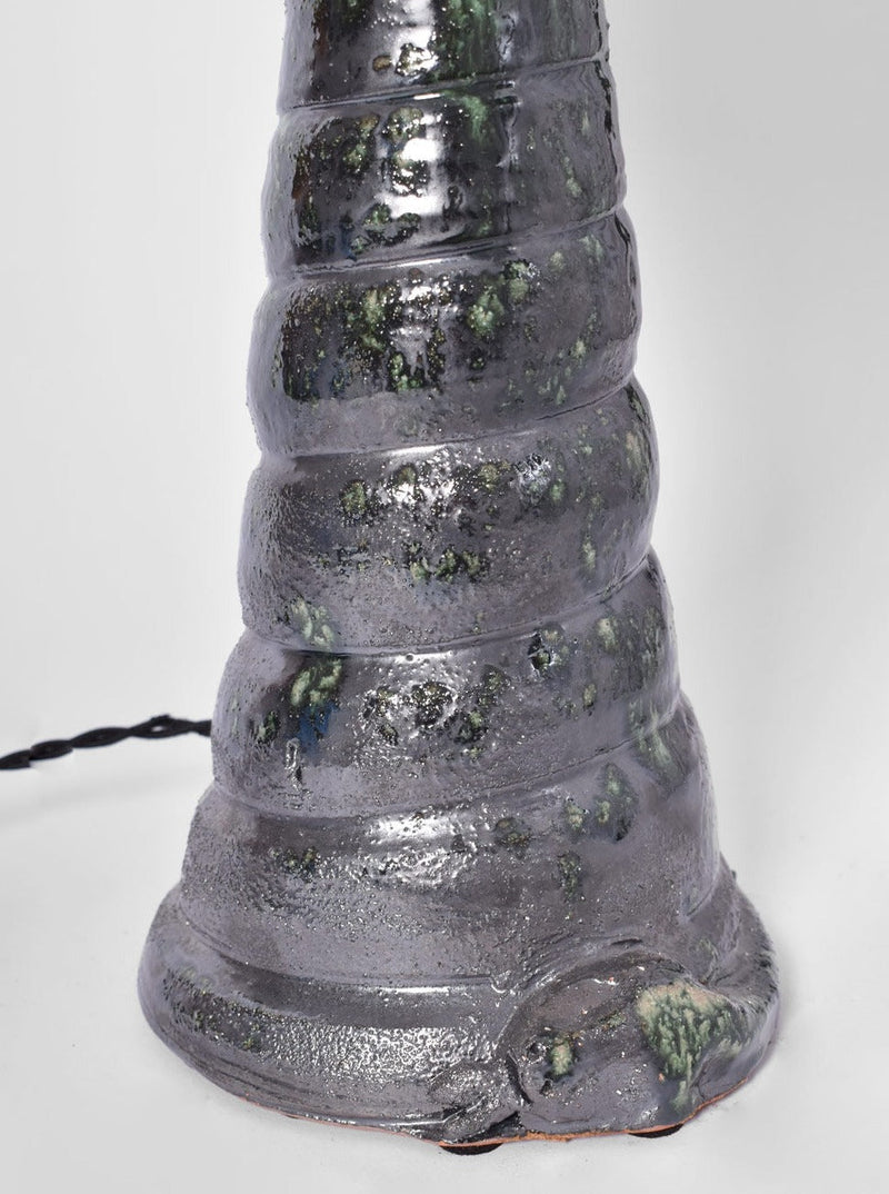 A close-up of the base of the "Teotihuacan" Green Ceramic Table Lamp by Barracuda Interiors, Barracuda Edition, featuring a textured, ridged green ceramic surface with a glossy, mottled gray glaze and a modern black power cord.