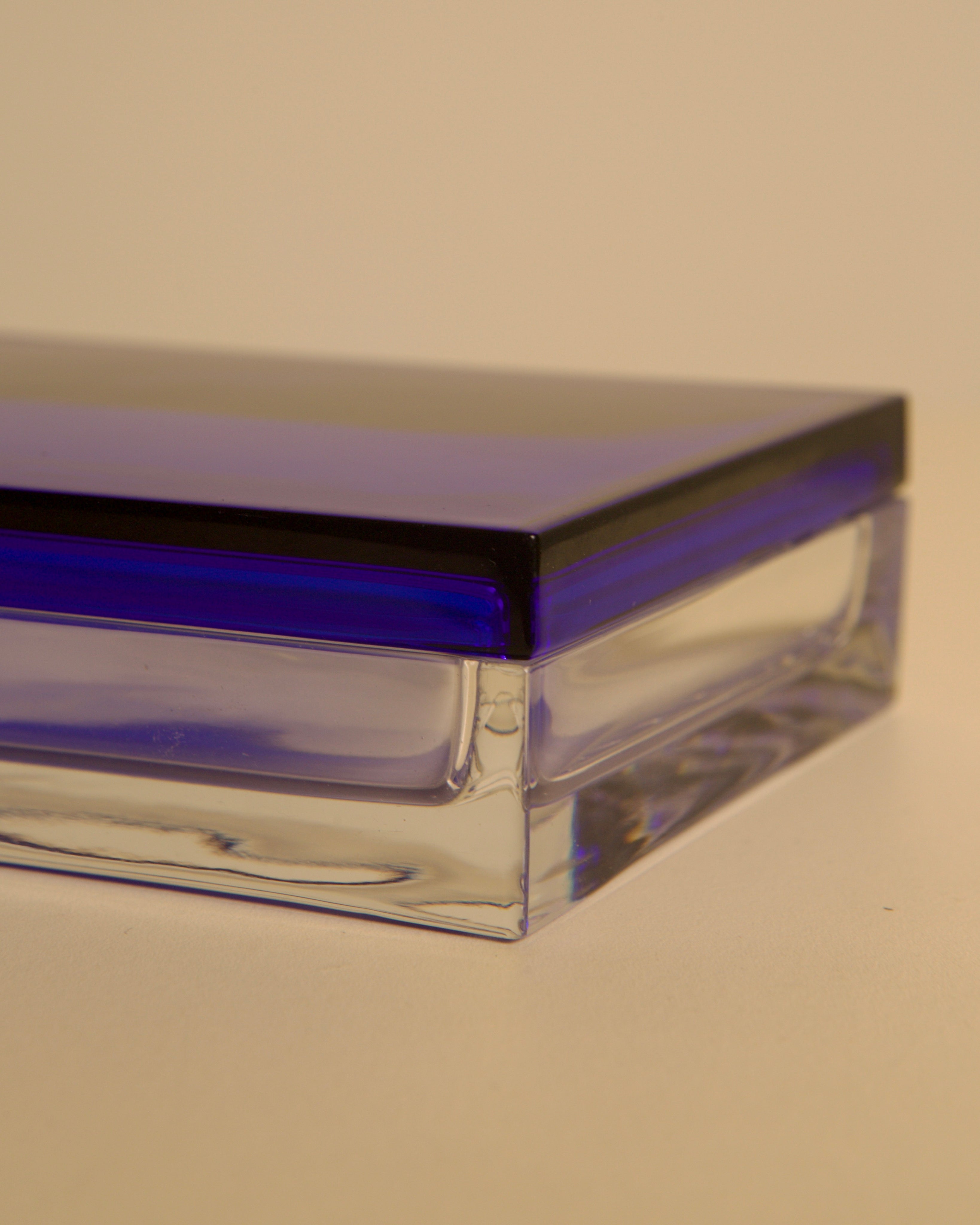 A close-up of the Italian Box in Transparent and Blue Crystal by Duccio Di Segna, 80's, for Treaptyque—rectangular with a clear base and deep blue lid—evoking 1980s Italian design, set against a plain beige background.