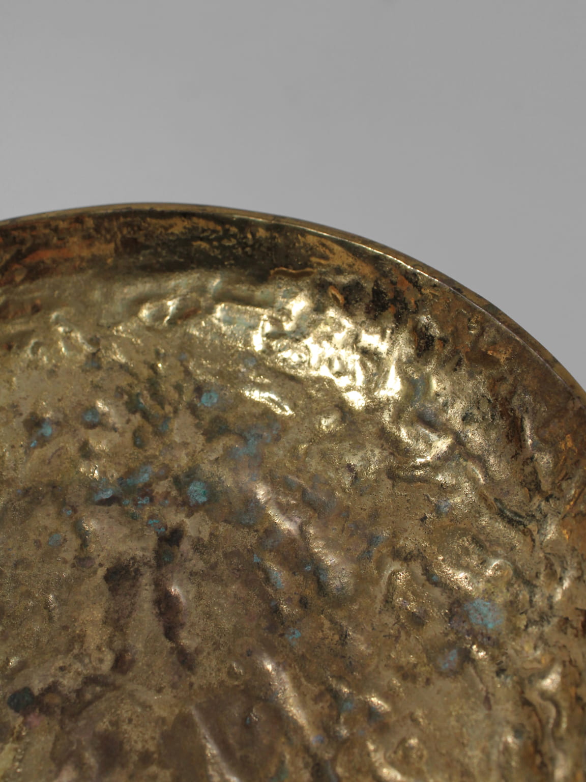 A close-up of the Massive Organic Textured Brass Bowl by Vintage Stories highlights its glossy, textured surface with oxidation patches and a subtly uneven rim, evoking mid-century charm against a plain gray background.