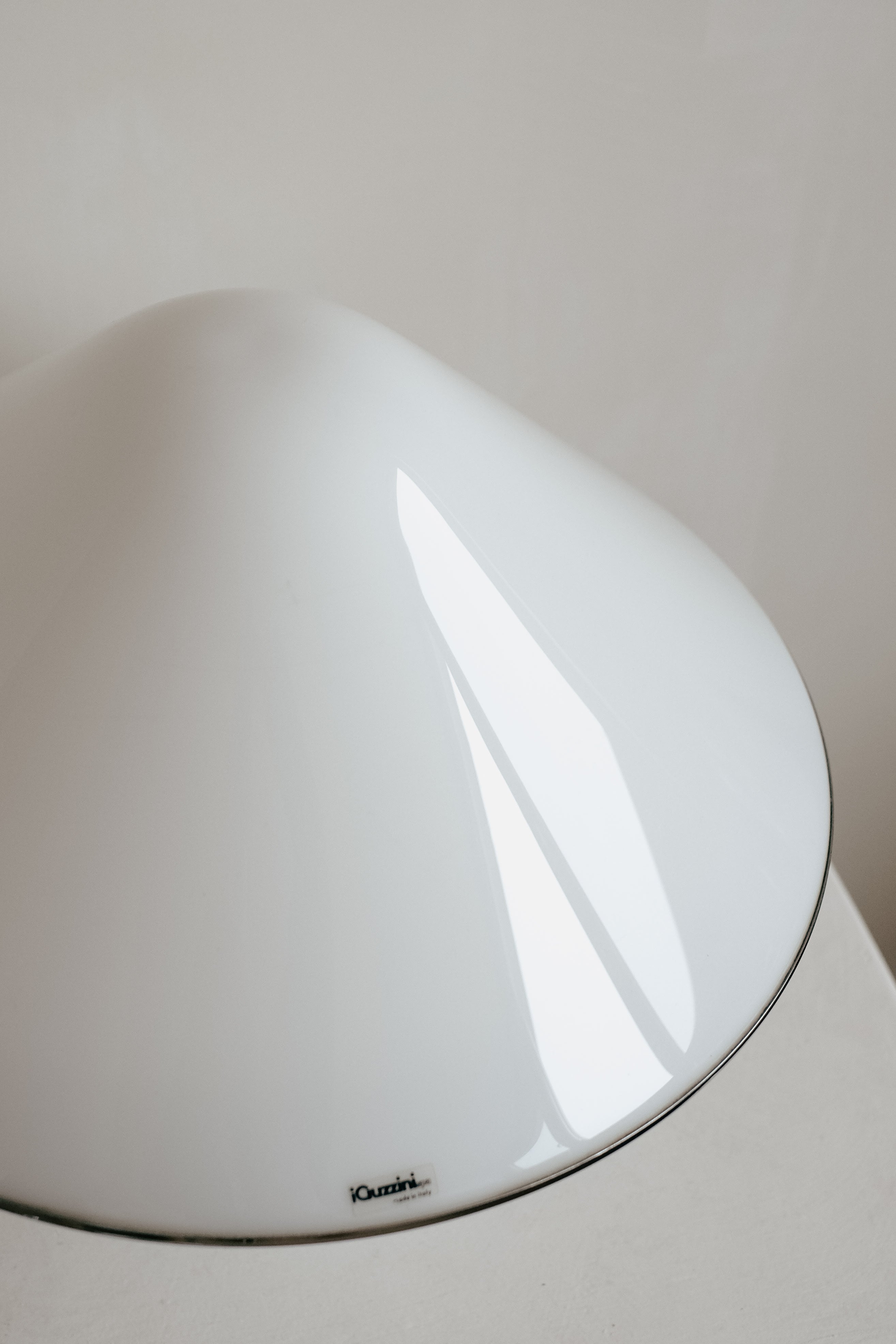 Close-up of a smooth, white, dome-shaped Harvey Guzzini Elpis Table Lamp with a glossy finish by septembre studios. Its elegant, vintage-inspired design stands out against a minimalistic neutral background.