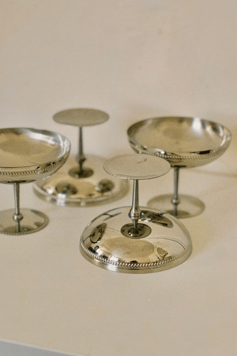 The Set of 4 Silver Ice Cream Coupes by Manushi features three upright and one upside down on a light surface, highlighting their reflective finish and elegant beaded rims.