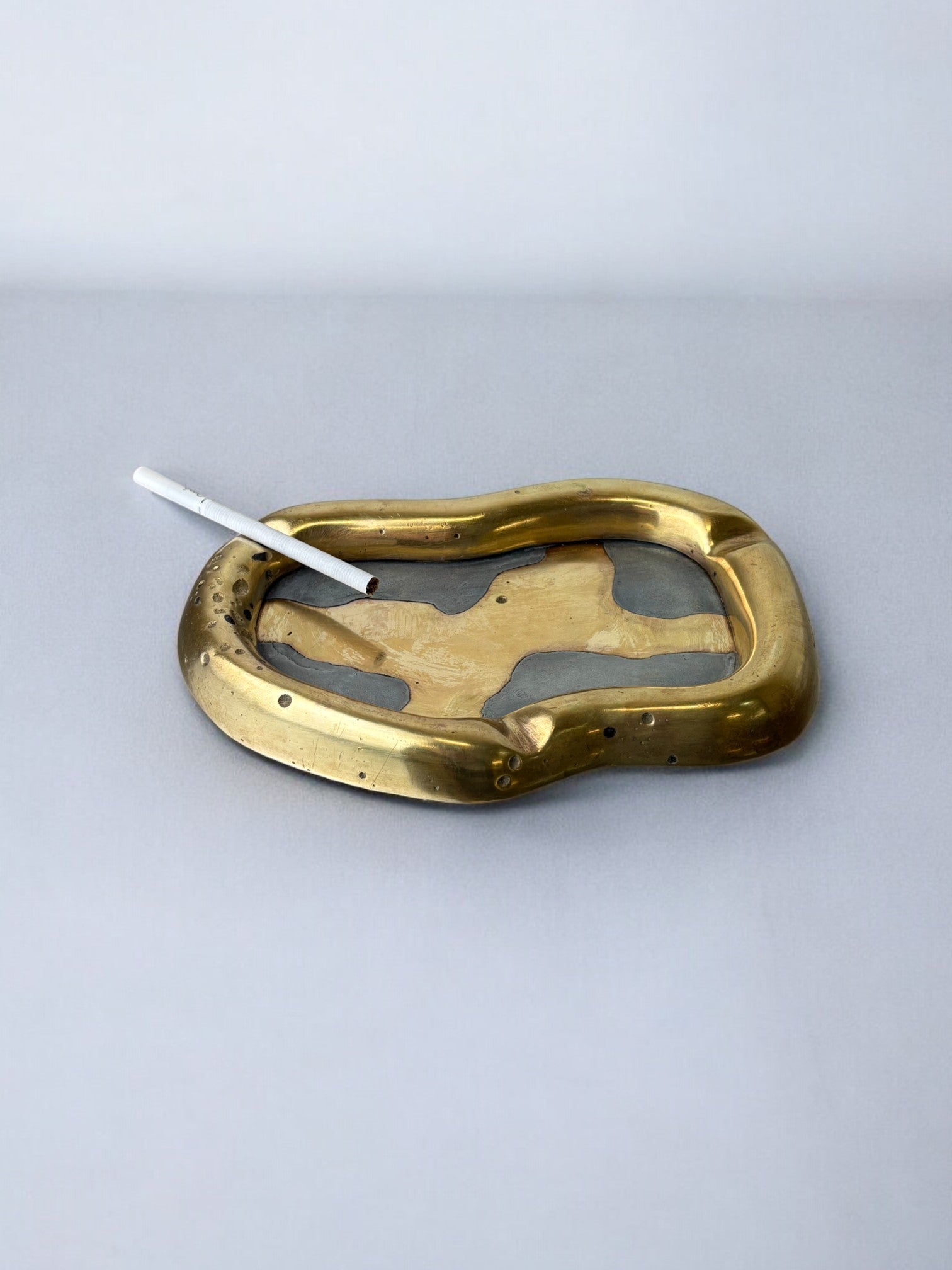 Brutalist ashtray by David Marshall, Spain, 70's — close-up of brass surface with cigarette