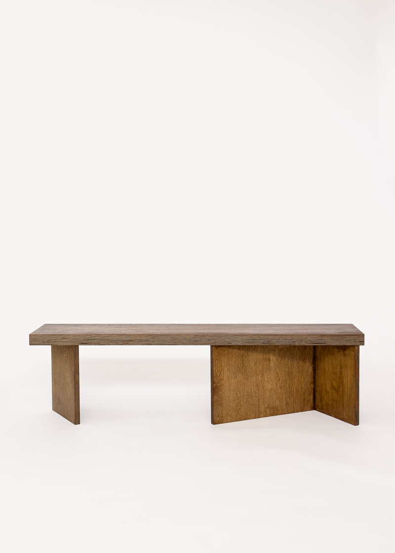 The Free plan Bench by GOONS features a minimal wooden design with a flat rectangular seat and two flat perpendicular legs, inspired by modern architecture, shown against a plain white background.