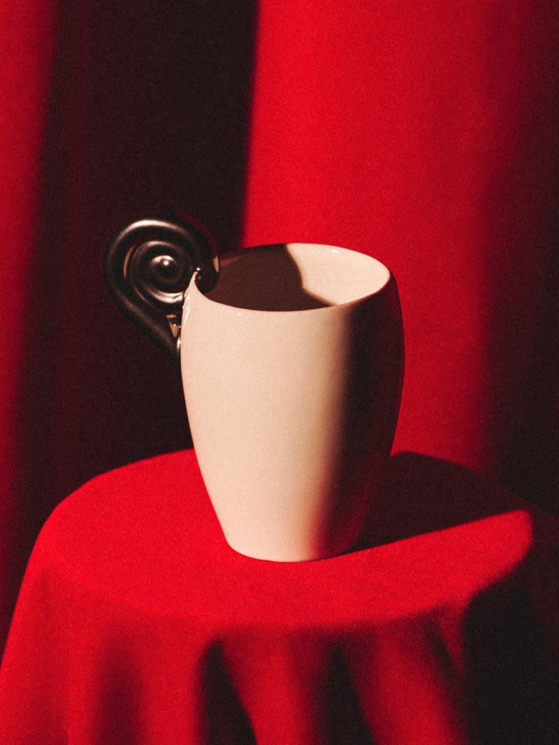 White ceramic Aries cup with platinum spiral horn handle on red surface