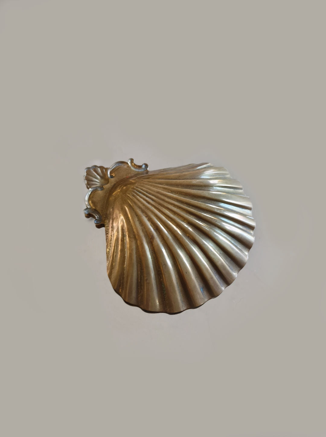 The Les Objoies Shell Brass Vide Poche, featuring a scalloped texture, rests elegantly on a plain off-white background.