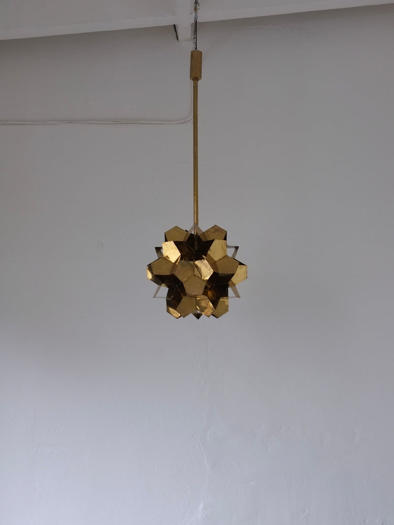 The Brutalist Brass Chandelier by Veter Vintage, a 1970s Latvian design, hangs from the ceiling against a plain white wall, creating a modern and minimalistic look.