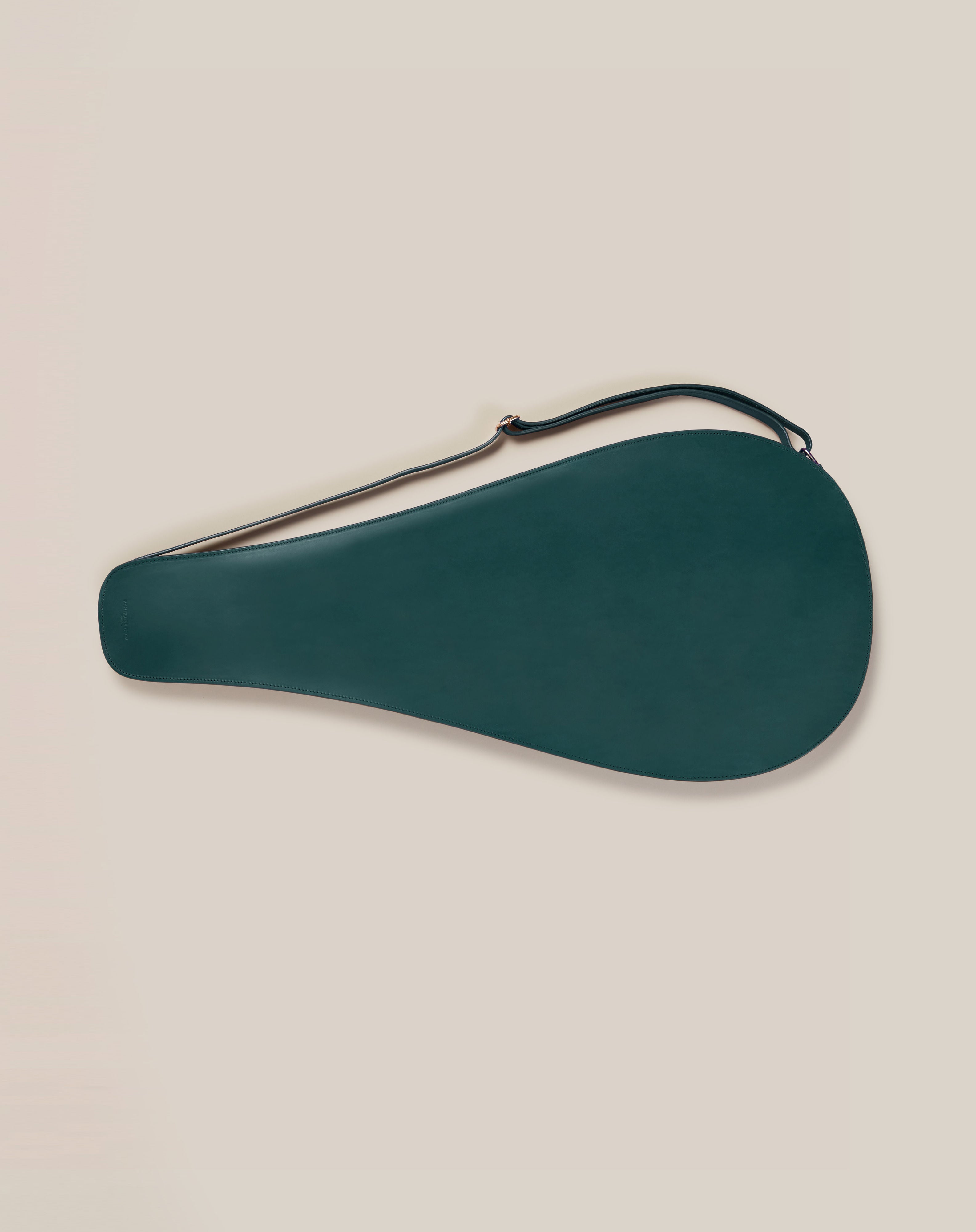 Set against a light beige background, the Leather Tennis Racket Cover by Paradise Row is a dark green, teardrop-shaped accessory crafted from sustainable vegetable-tanned leather with a long strap.