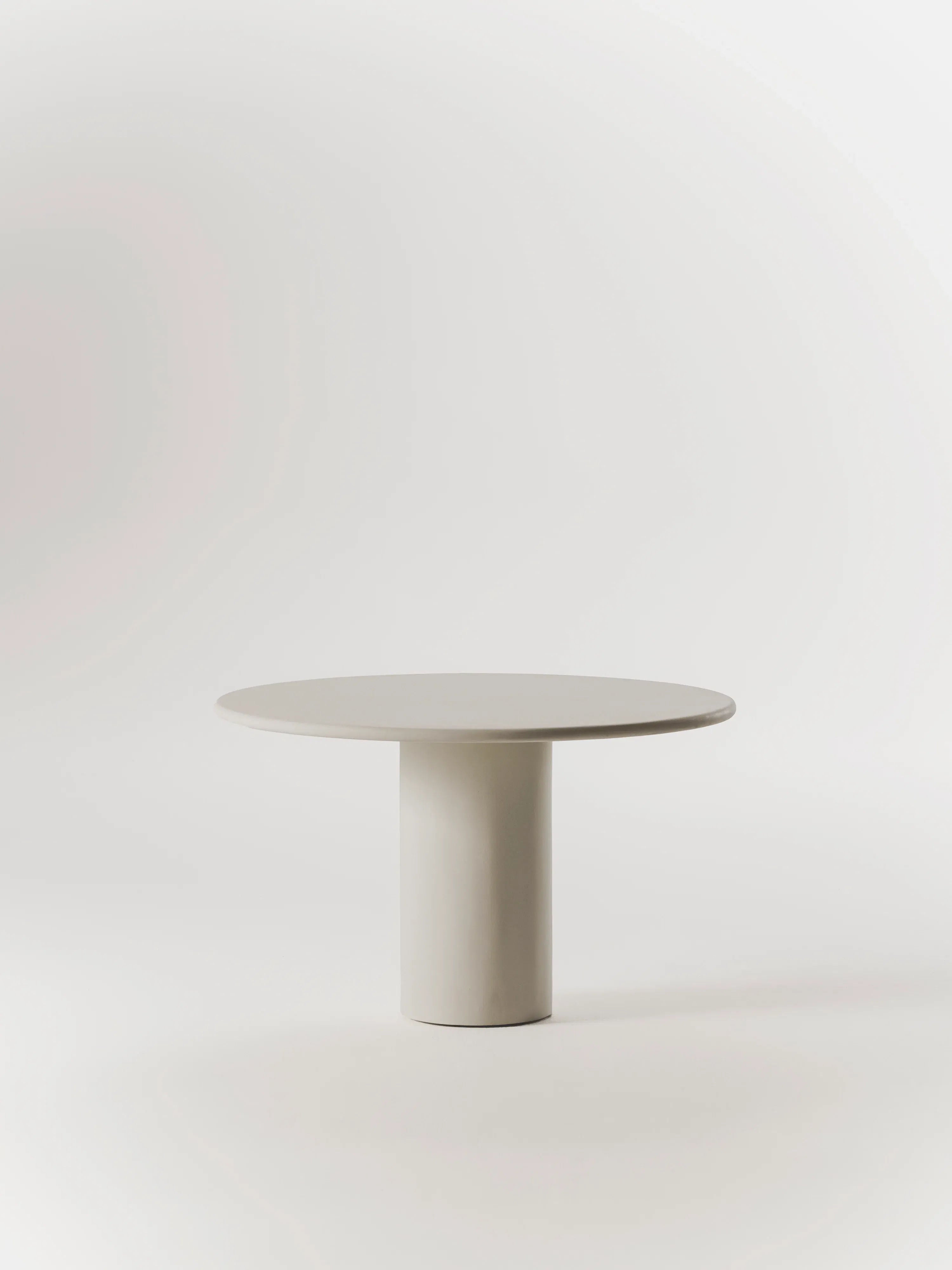 The Gio Dining Table by MarlotBaus is an elegant, minimalist piece with a smooth white surface and cylindrical base that exudes sophistication against a light background.