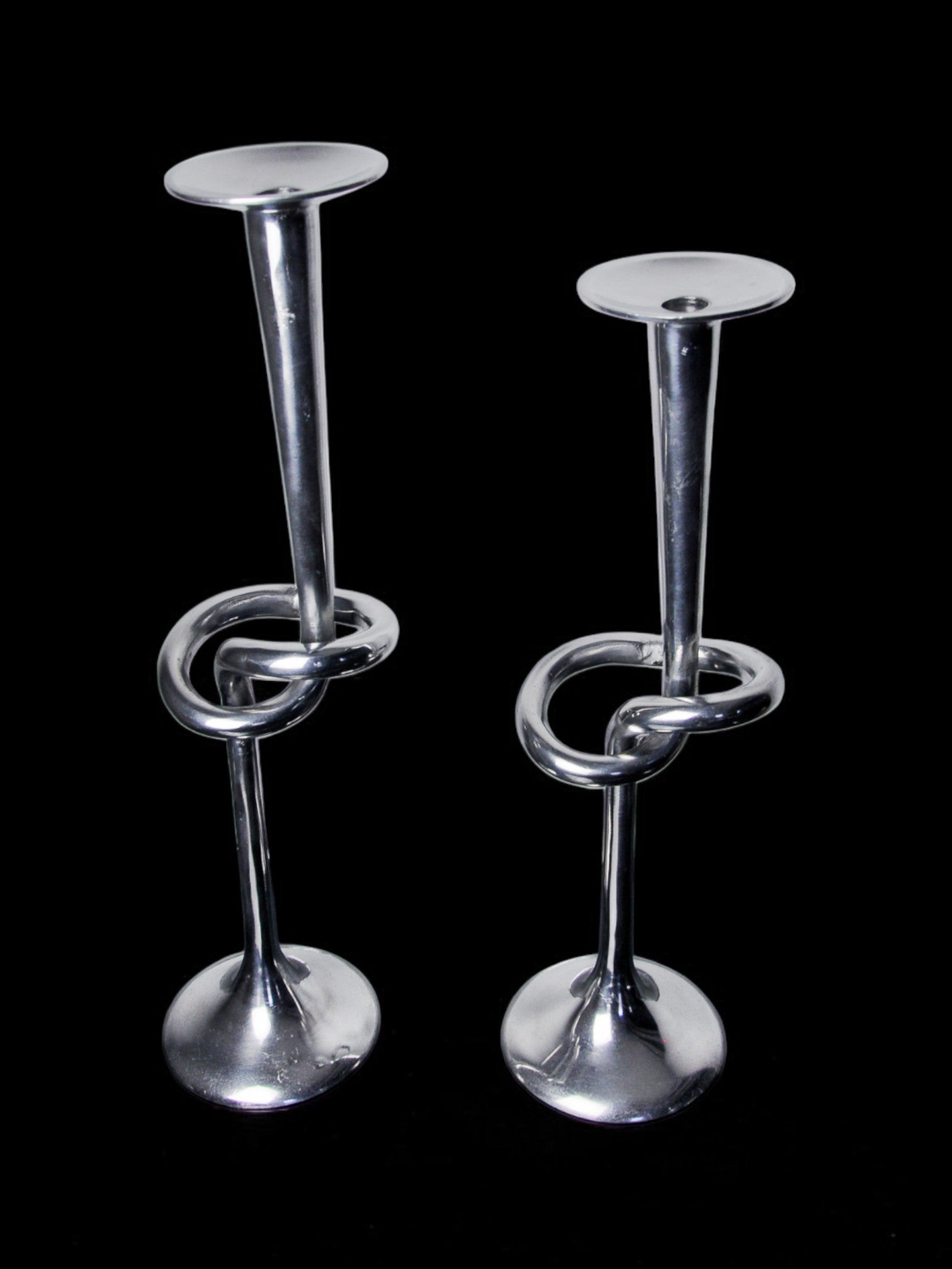 A pair of XL knotted aluminum candlesticks by Malamar Studio, Italy, 1980, feature twisted stems and showcase elegant Italian design and craftsmanship against a black background.