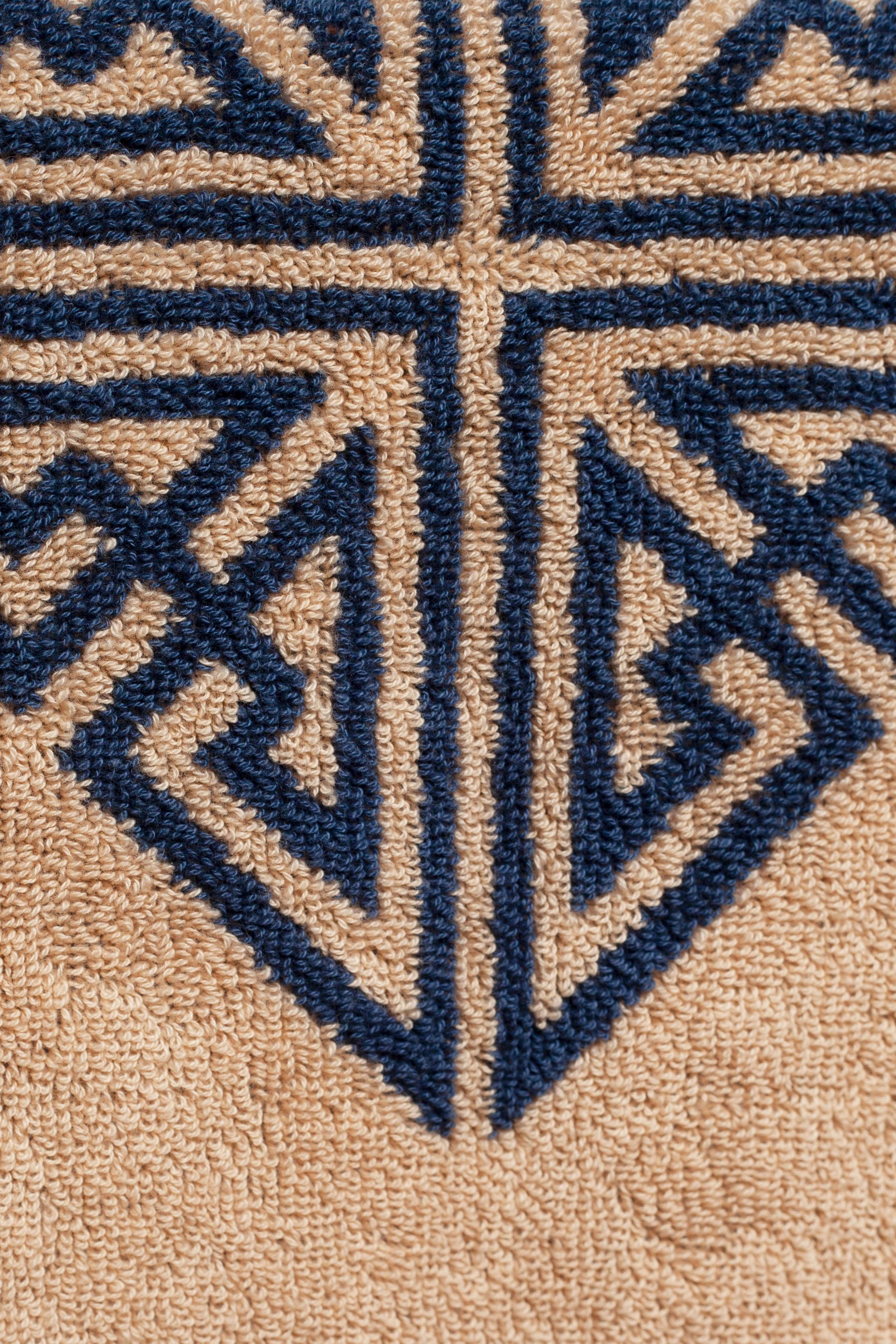 Close-up of an Agnes Hand Towel by Autumn Sonata with a geometric pattern in blue and beige colors, showing part of an embroidered or woven design.