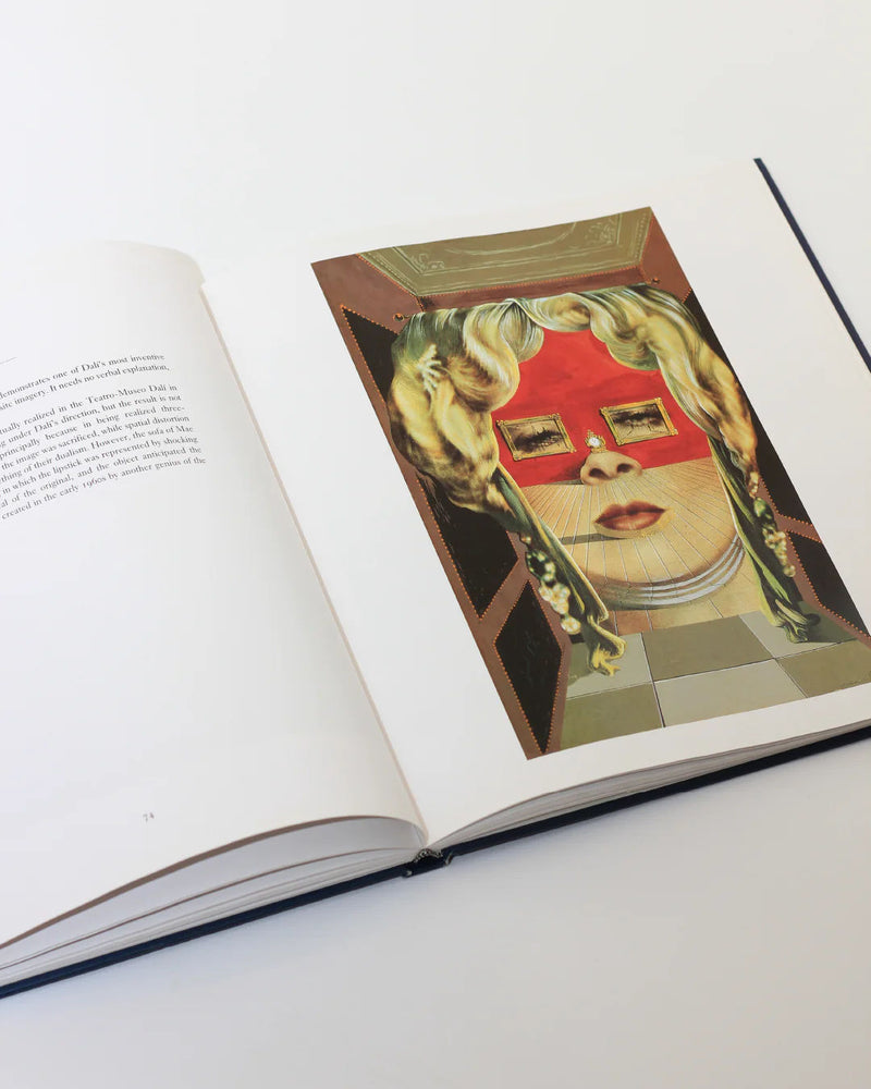 An open copy of Dali The Masterworks Book from Boga Avante Shop showcases a surreal collage reminiscent of Salvador Dalí: a woman's face with a red mask overlay and blonde hair framed by abstract geometric shapes in modern art style.