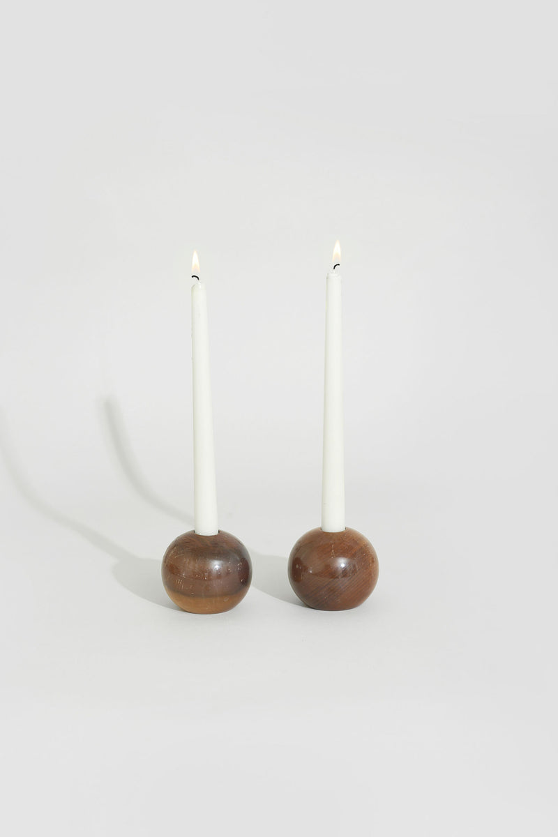 Two lit white taper candles in spherical walnut wood holders
