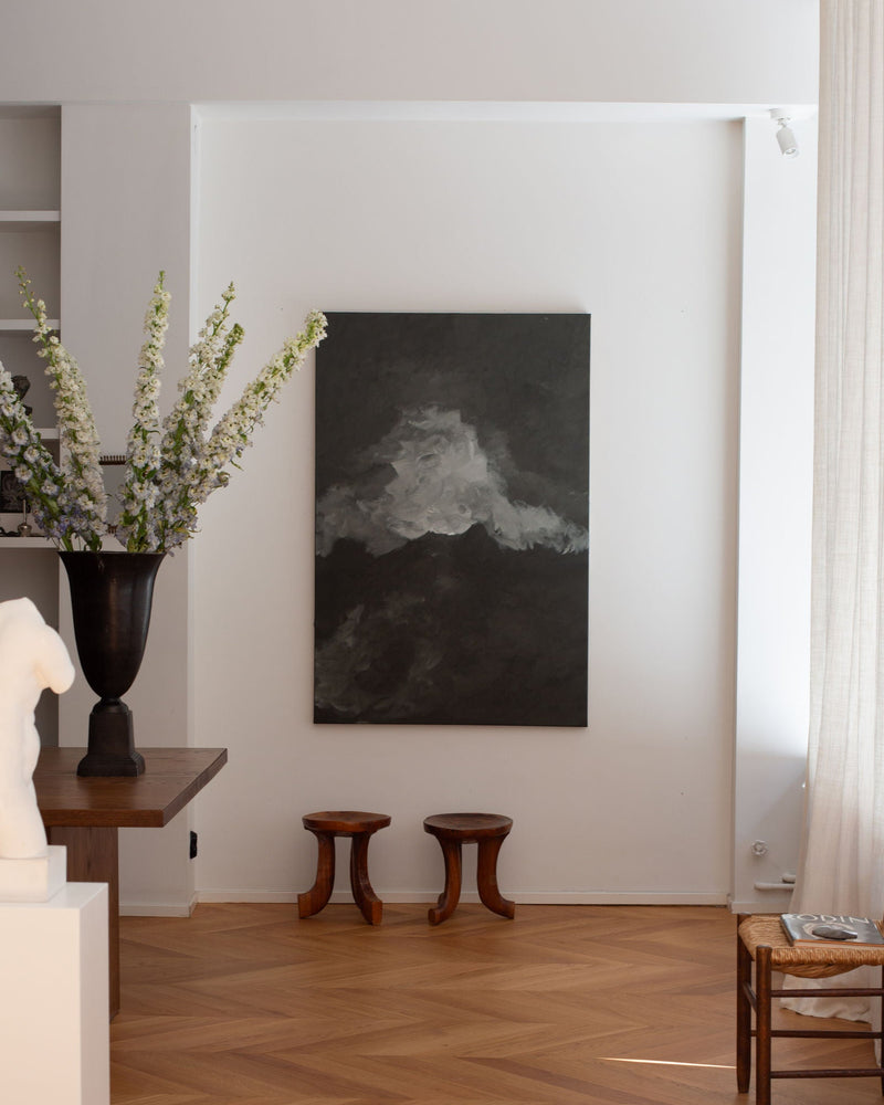 Abstract dark landscape painting with white clouds displayed in modern white interior