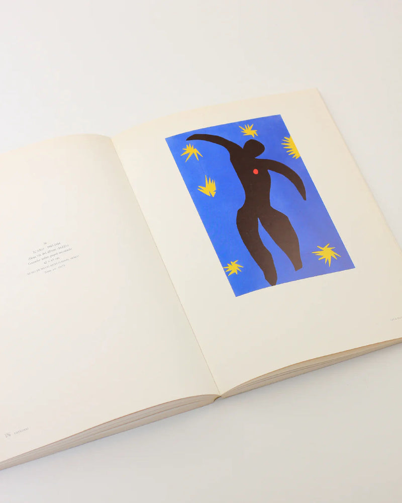 The Henri Matisse Book from Boga Avante Shop features an open page showcasing abstract artwork inspired by Matisse himself, with a black silhouette set against a blue backdrop adorned with yellow star-like shapes. The adjacent page includes minimal text, perfectly embodying the vibrant essence of modern art and Fauvism.