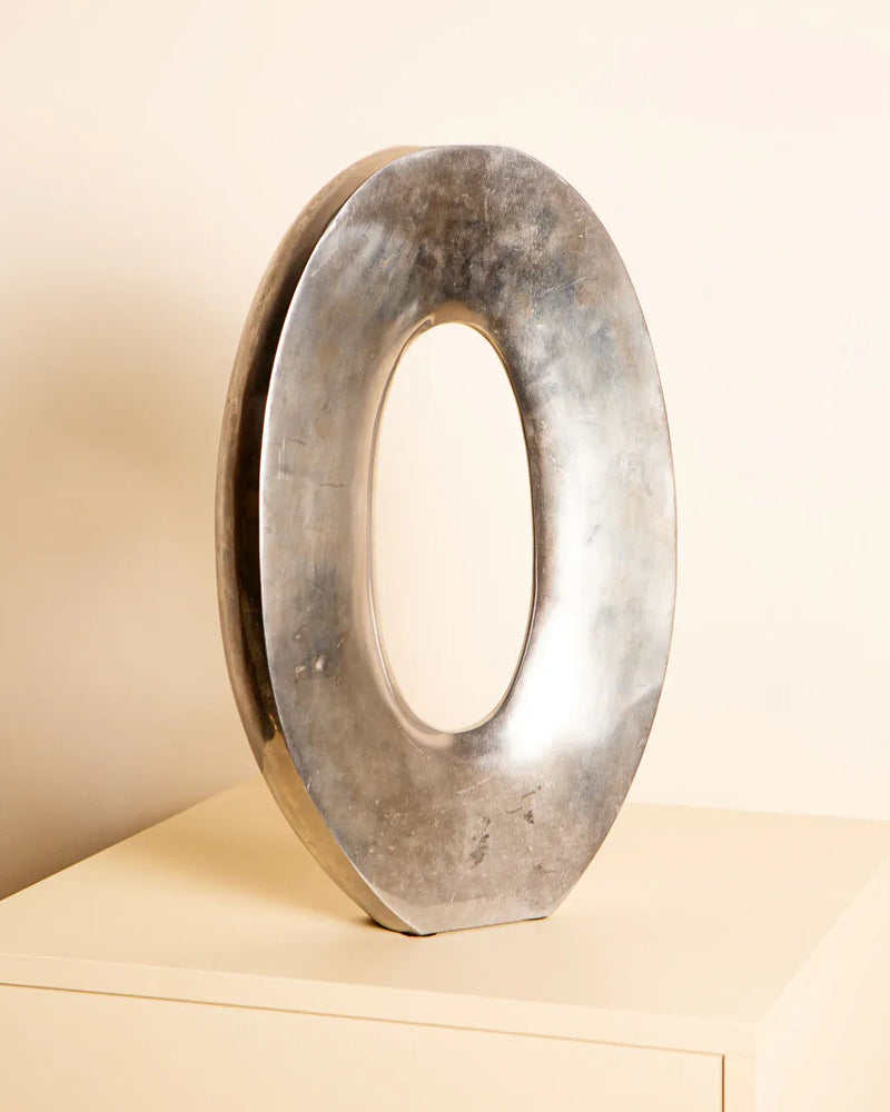 The Treaptyque Large Cast Aluminium "Oval" Vase 80s, a shiny silver masterpiece, stands upright on a light surface against a plain background. Its hollow center and modern oval shape showcase Italian craftsmanship and timeless elegance.