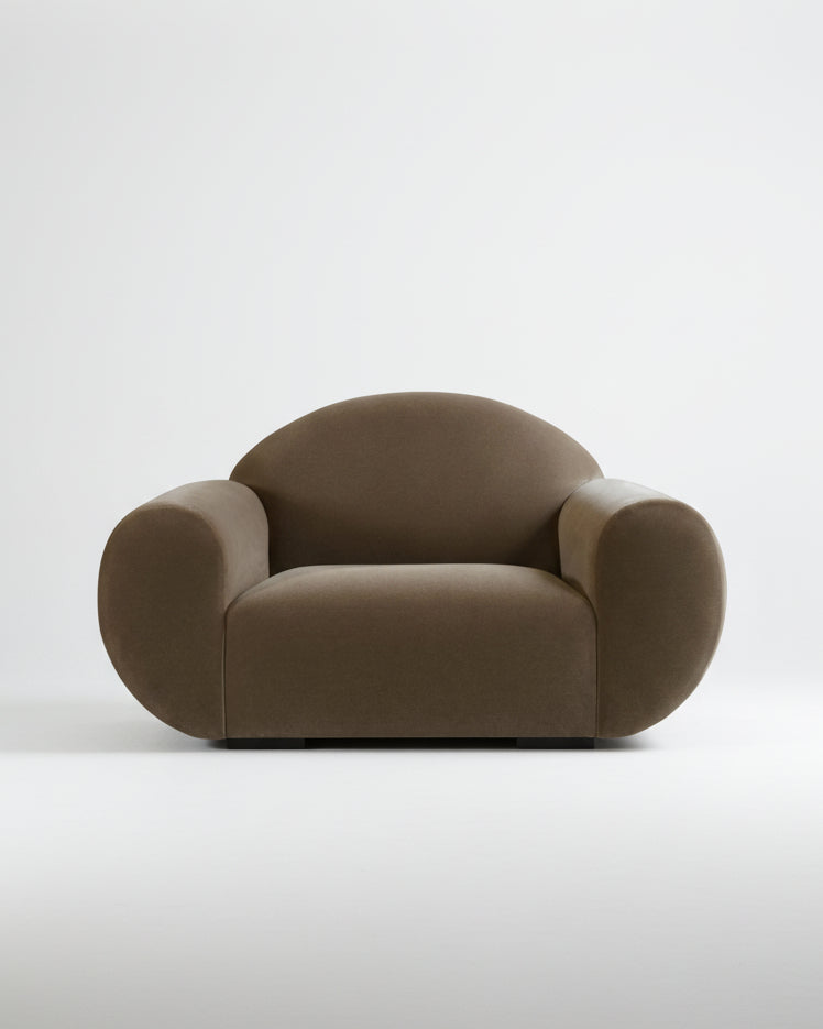 The "Sparta" Armchair by Ransom & Dunn features a contemporary round design with a dark brown mohair velvet finish, showcasing oversized plush arms and a rounded backrest. Placed against a light gray backdrop, this minimalist piece includes a smooth cushioned seat and black block feet.