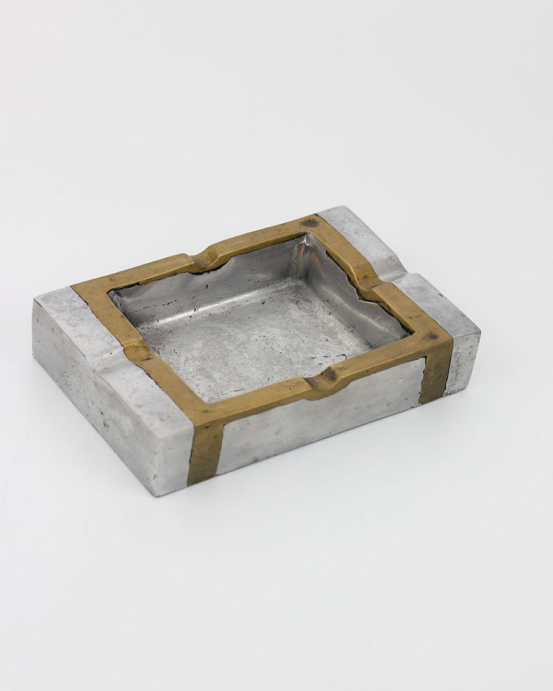 Brutalist Ashtray 70s by Boga Avante Shop: a rectangular metallic ashtray with a silver base, gold-edged detailing, and four cigarette rests. Inspired by brutalist design and crafted in Spain.