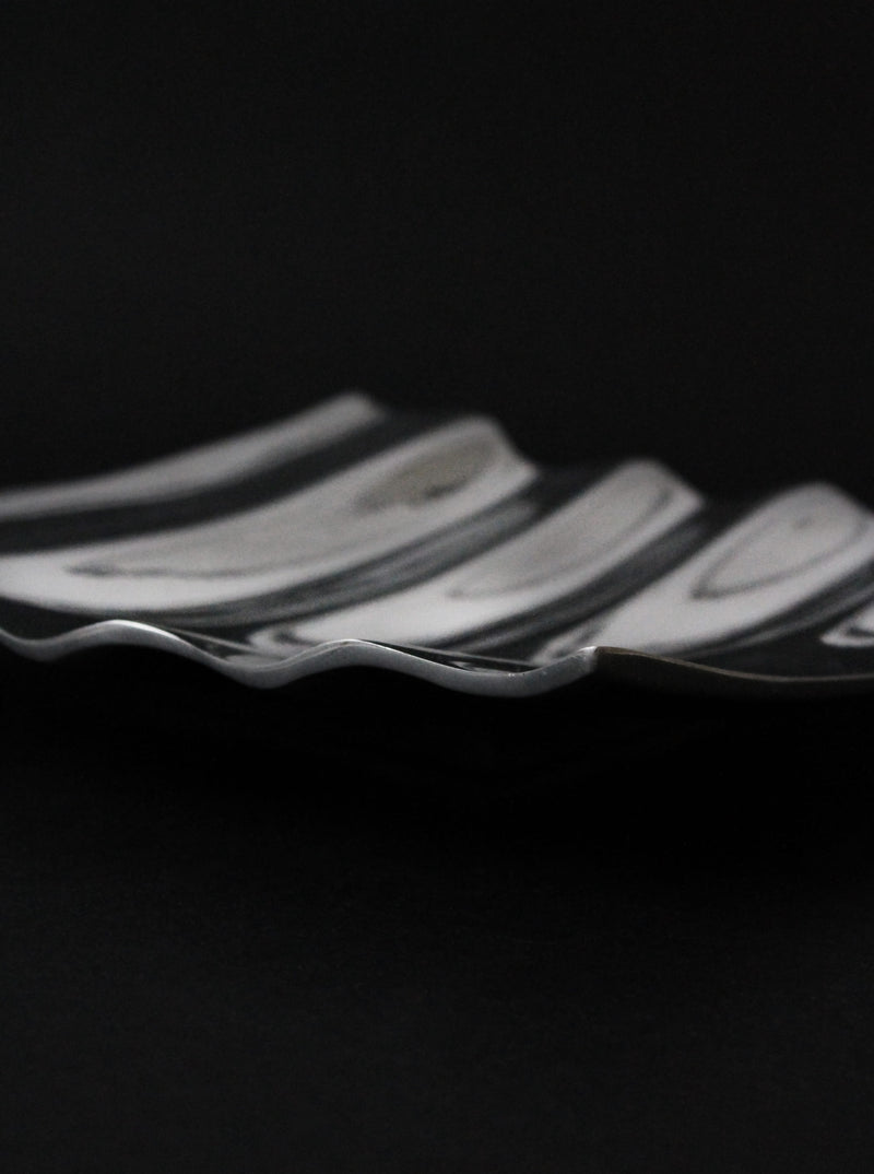 A close-up of the Vintage Stories Polished Aluminum Wave Bowl, featuring wavy edges and a sleek striped design, set against a dark background.