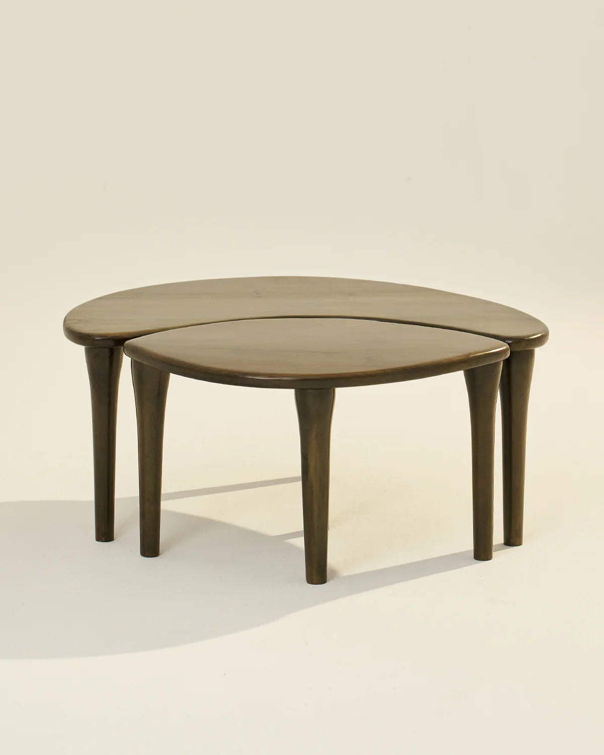 The LMNOH Crescent Coffee Table set features two nested tables with smooth, dark ashwood tops. The larger table is circular, and the smaller is crescent-shaped, creating a cohesive, space-saving design. Both have four tapered legs for stability and style.