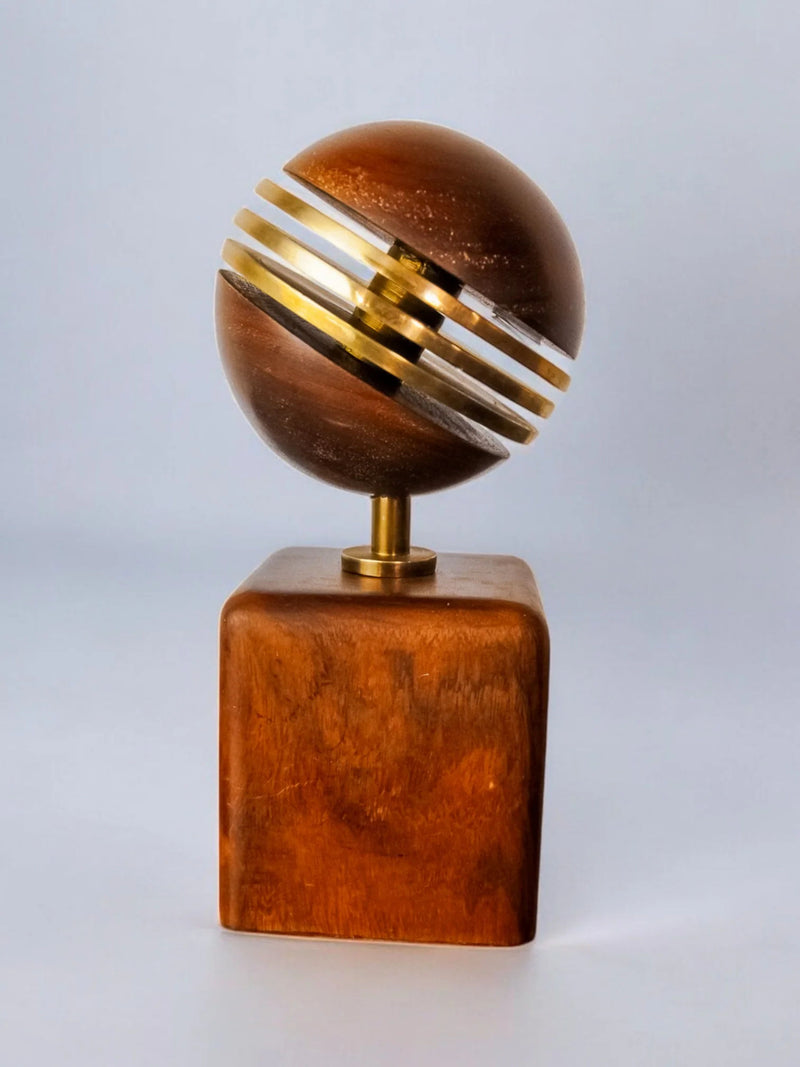 The Brutalist Paperweight by Ardisur, Spain 1970 from Malamar Studio is a wooden trophy with a spherical top adorned with golden metal bands on a square base, set against a light background, showcasing elegant simplicity.