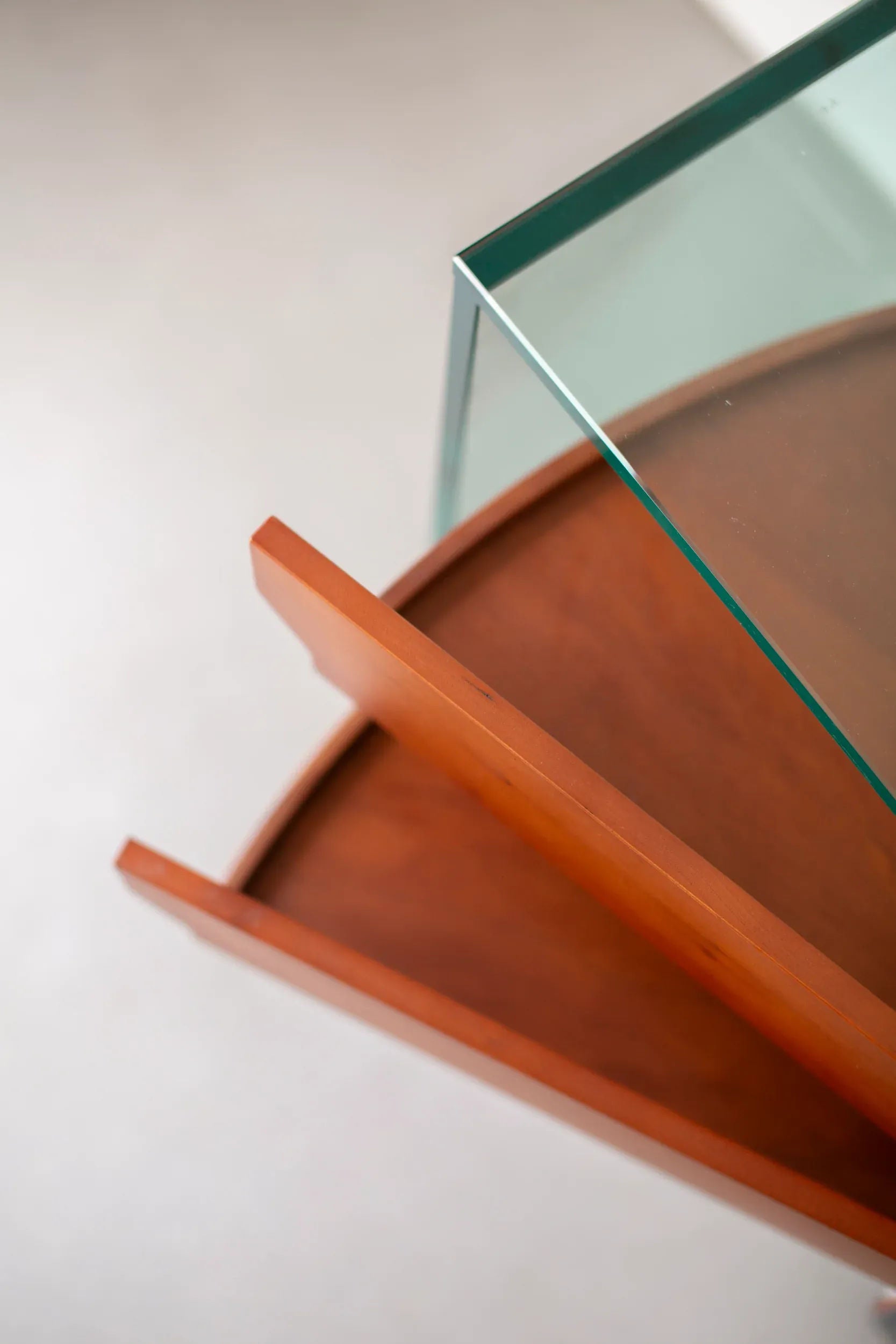 Close-up of a modern spiral staircase with wooden steps and a tempered glass railing. The image, evocative of the Tonelli Camicino Cabinet designed by Marco Gaudenzi for CU-RA-TED, is taken from an angle above, highlighting the sleek contrast between the warm wood and the clear glass. The background is out of focus.