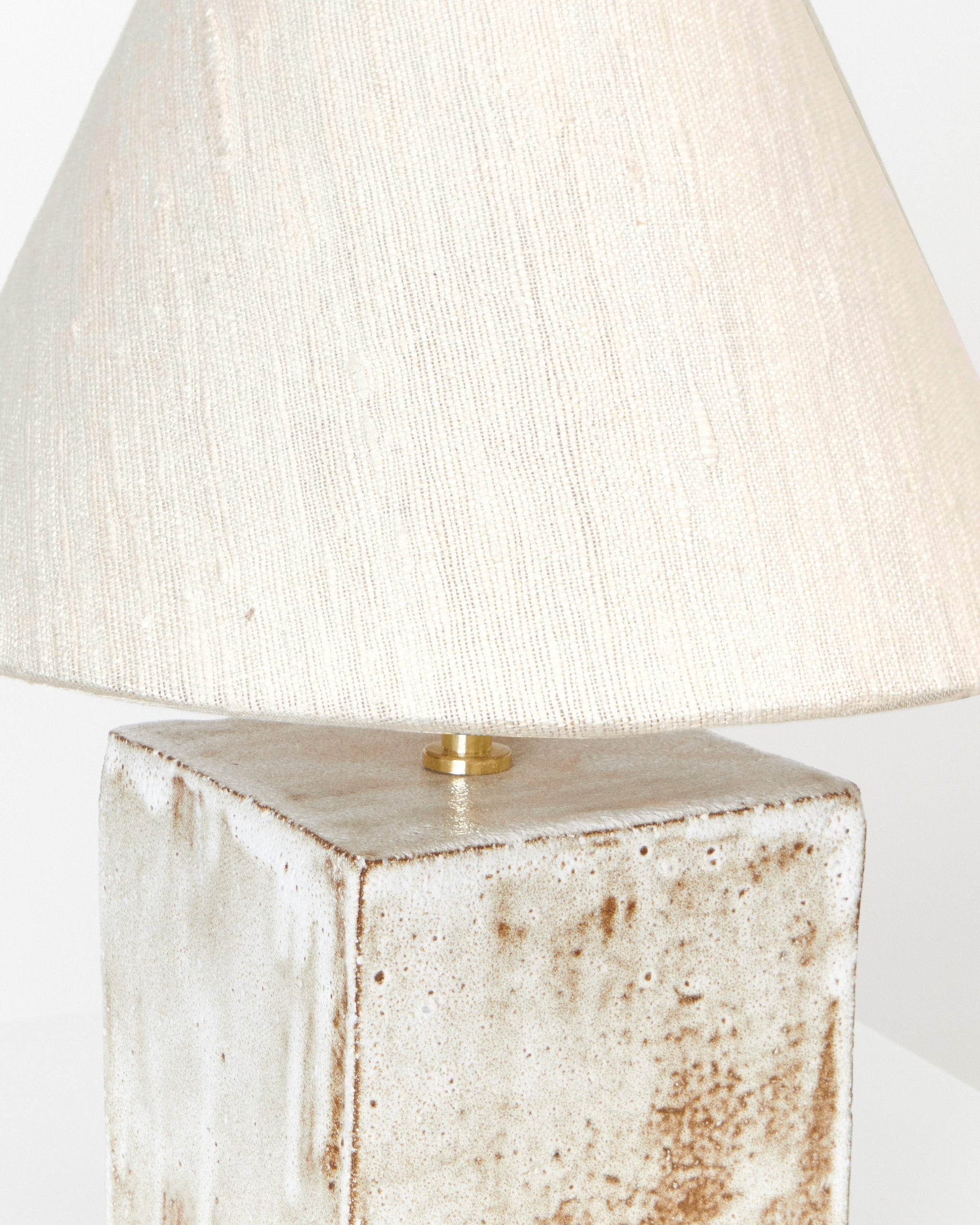 A close-up of the Arouca Table Light Coral White by Project 213A, featuring a handmade, textured off-white square ceramic base with brown speckles, a large cream fabric shade, and a small gold accent on top.