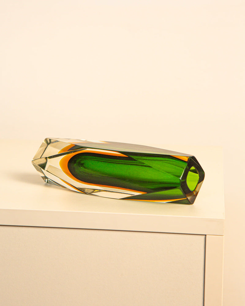 A Parrot-green “Diamond” Vase by Flavio Poli from the 80's, by Treaptyque, rests horizontally on a white cabinet against a plain beige background.