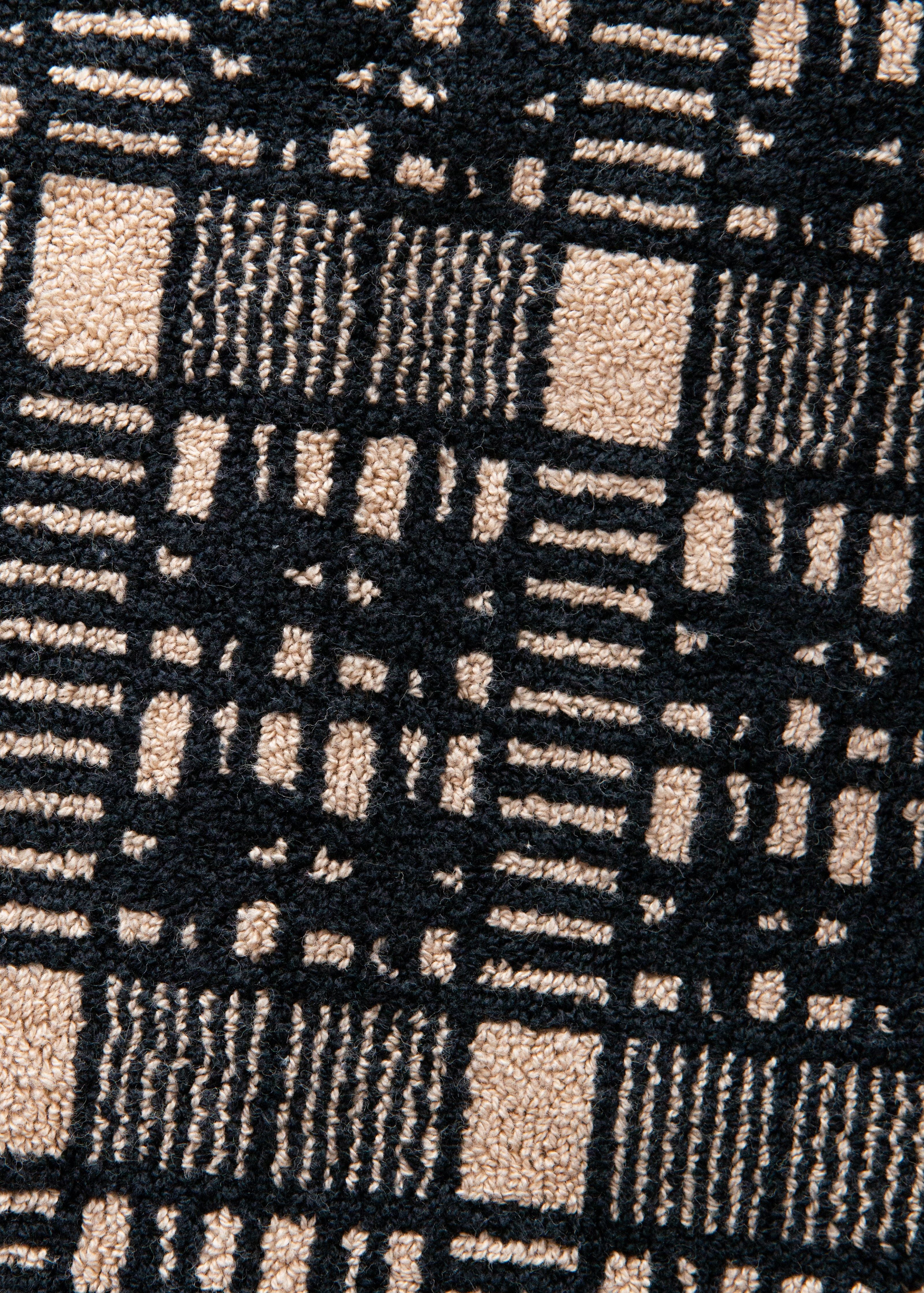 Close-up of an Alma Bath Sheet towel from Autumn Sonata with a geometric pattern, featuring alternating black and beige squares and lines.