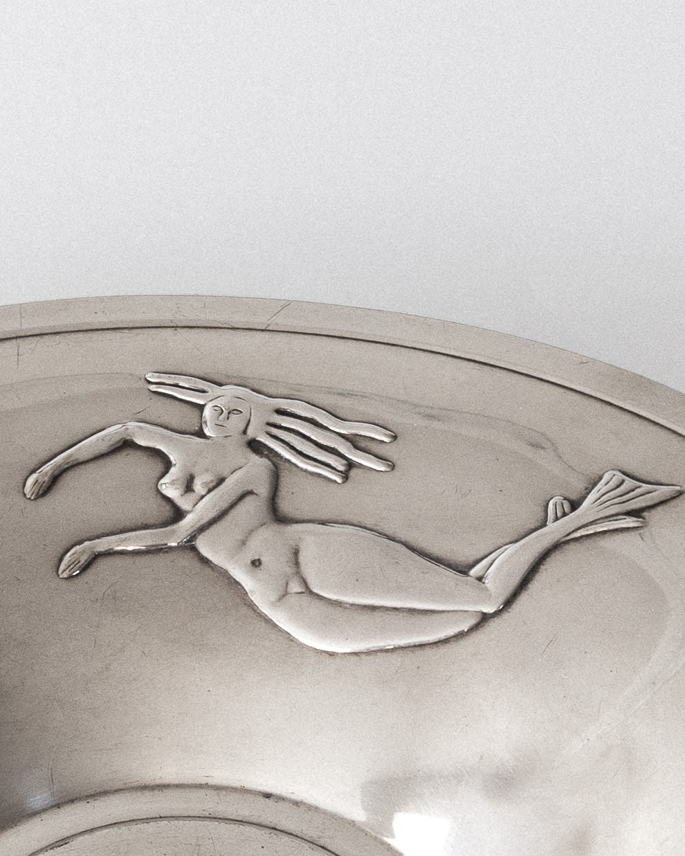 A close-up of the Spigel Decorative Silver-Plated Dish from 1930s Sweden shows an embossed Art Deco mermaid with flowing hair and a curved tail, swimming left. The bowl's reflection enhances its intricate details.