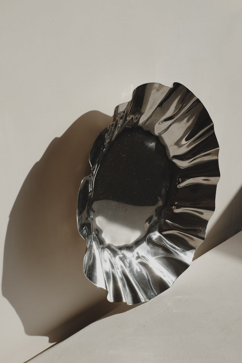 Polished chrome decorative bowl with dramatic ruffled edges casting shadow