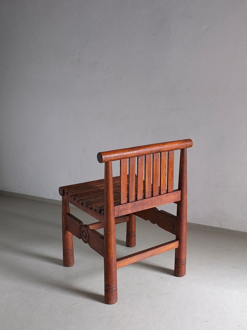 A Carved Oak Low Back Chair by Veter Vintage, originating from France in the 1960s, stands on a plain, light-colored floor against a textured, neutral wall. The chair features a minimalist design with vertical slats for the backrest and sturdy cylindrical legs, complemented by subtle decorative carvings on the frame.