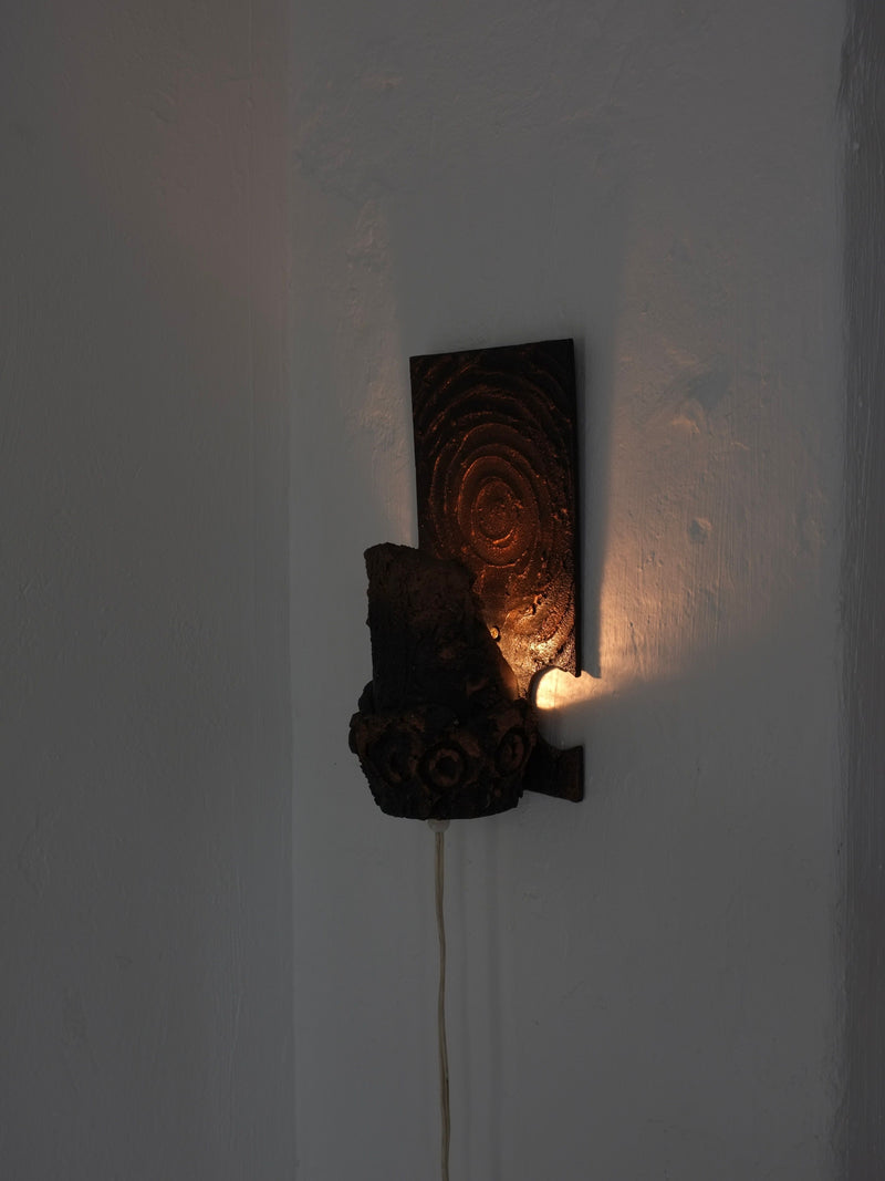 Illuminated brutalist ceramic wall sconce showing textural detail